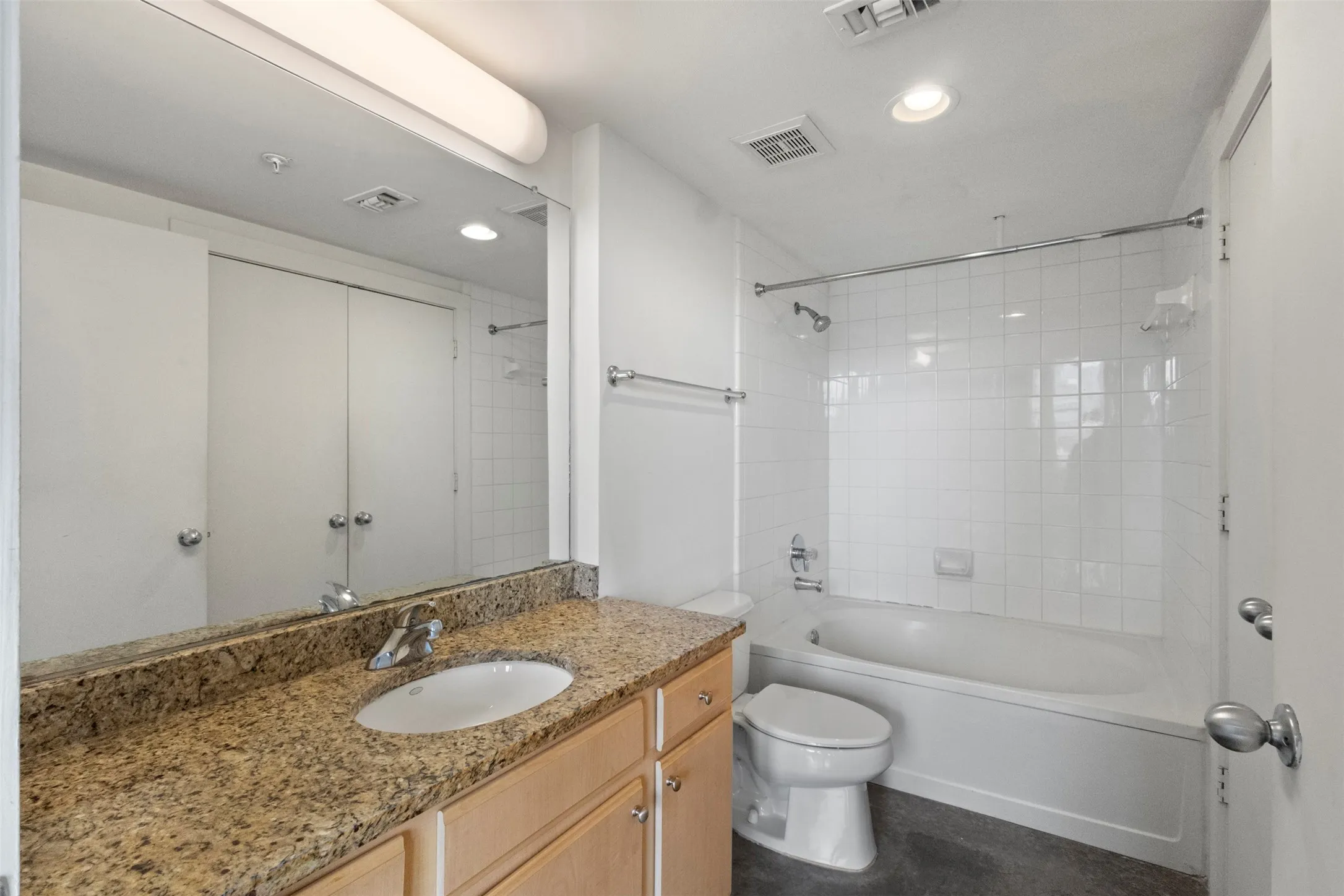 Bathroom featuring a vanity with a light-toned countertop and integrated sink, light wood cabinetry, and a full-width mirror