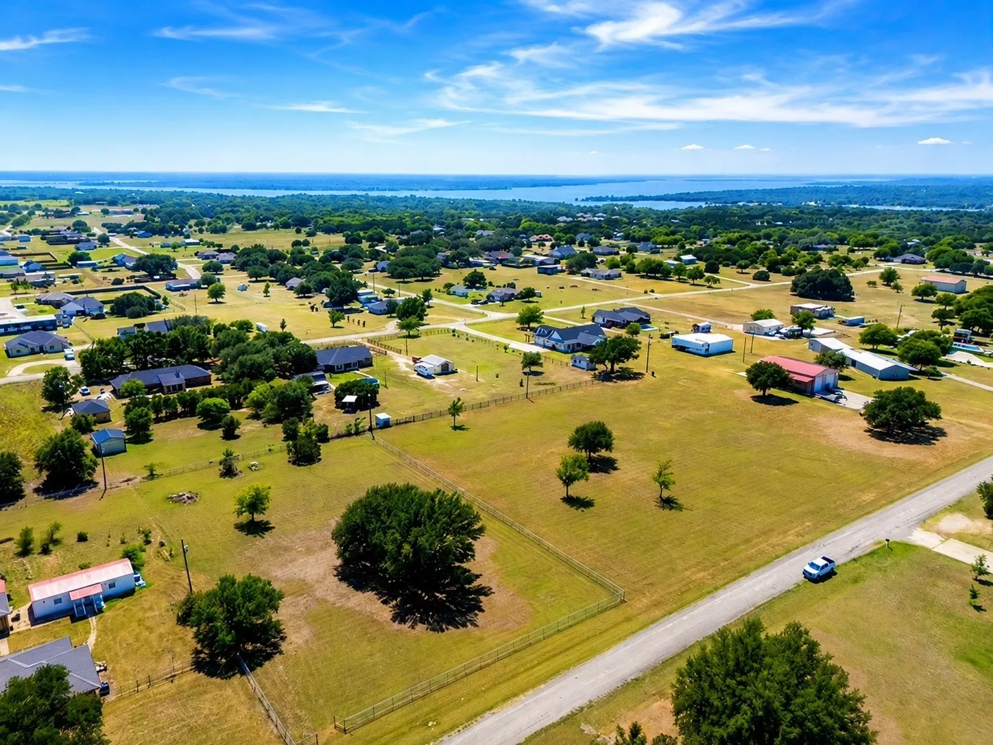 Expansive rural landscape featuring scattered residential properties, mature trees, and a distant body of water