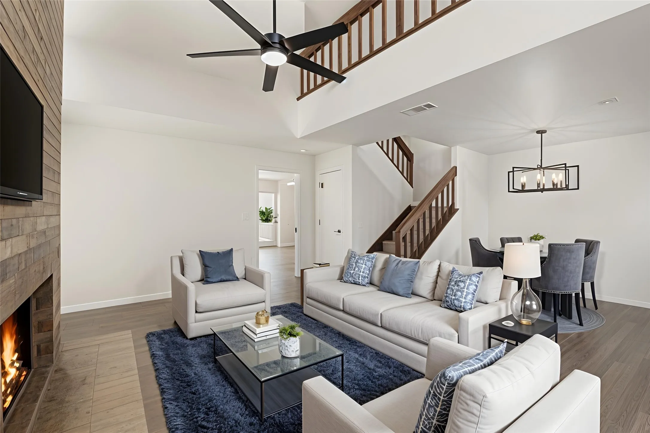 Vaulted ceiling with a large ceiling fan, wood-finish flooring, a contemporary fireplace with a stone surround, and an open-concept dining area with a modern chandelier