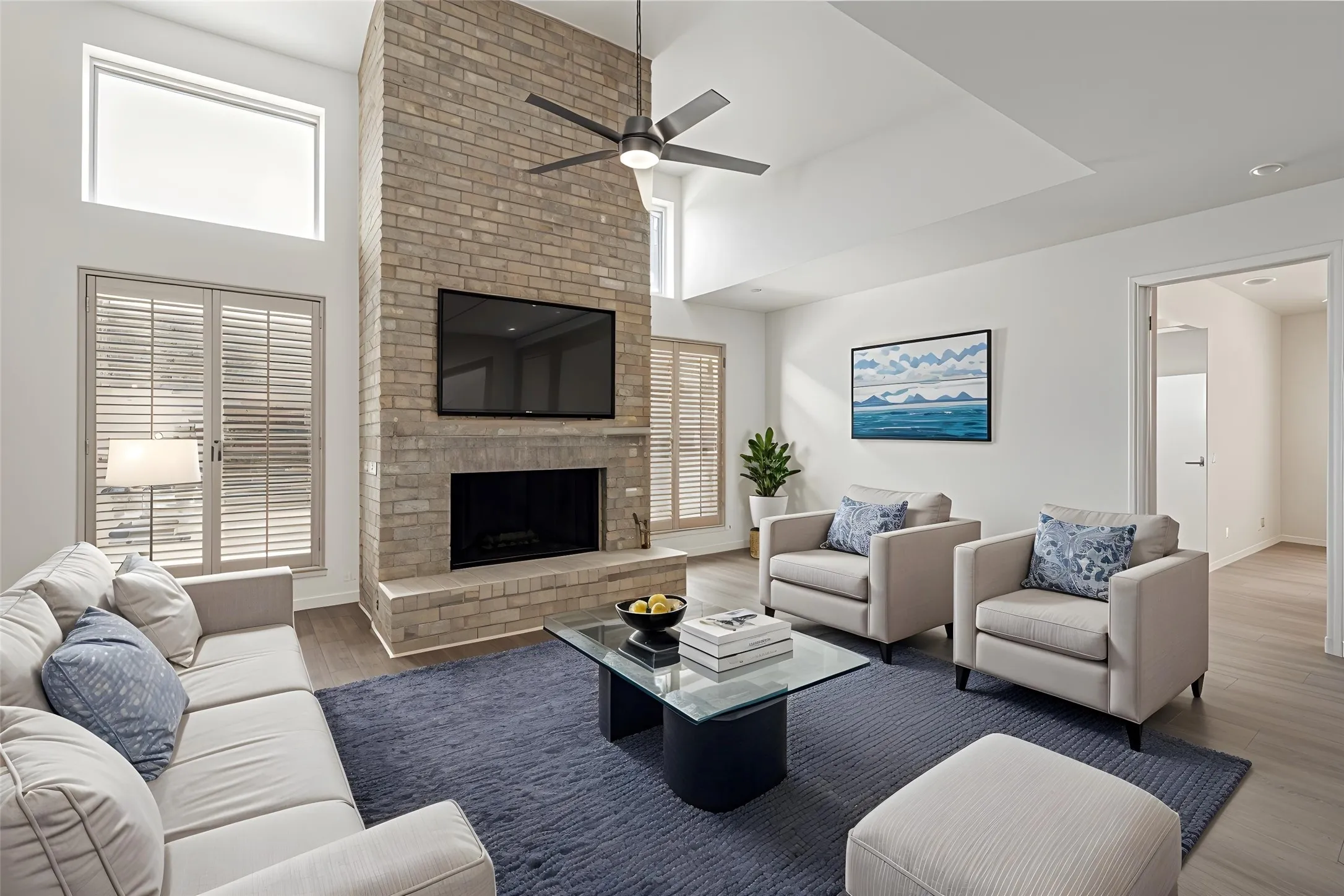 Two-story living area with a floor-to-ceiling brick-faced fireplace, vaulted ceiling, wood-finish flooring, and plantation shutters