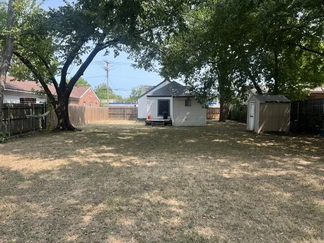 Expansive backyard featuring a wood privacy fence, mature shade trees, and a detached storage shed