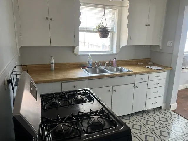 Charming kitchen featuring white cabinetry with ample storage, wood-finish countertops, dual-basin sink with faucet, and gas range with black cooktop