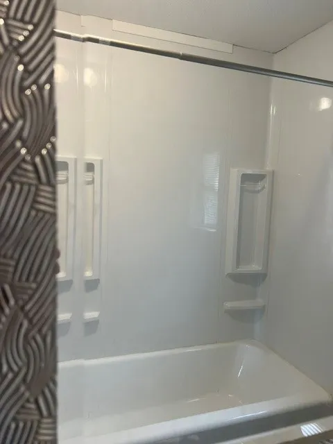 White bathtub and shower surround with integrated shelving and a chrome shower rod