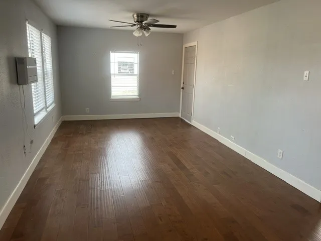 Spacious room featuring rich wood-finish flooring, neutral wall finishes, ceiling fan with integrated lighting, and abundant natural light from multiple windows