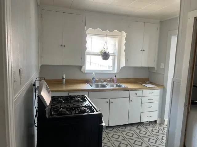 Charming kitchen featuring white cabinetry with ample storage, wood-finish countertops, a double-basin sink with faucet, and a gas range