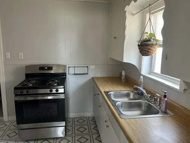 Efficient galley kitchen featuring stainless steel gas range with convection oven, dual stainless steel sink with chrome faucet, and wood-finish countertops