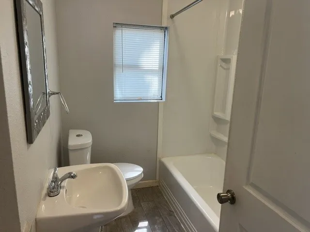 Efficient full bathroom featuring a pedestal sink with chrome faucet, toilet, and shower/tub combination with tile surround