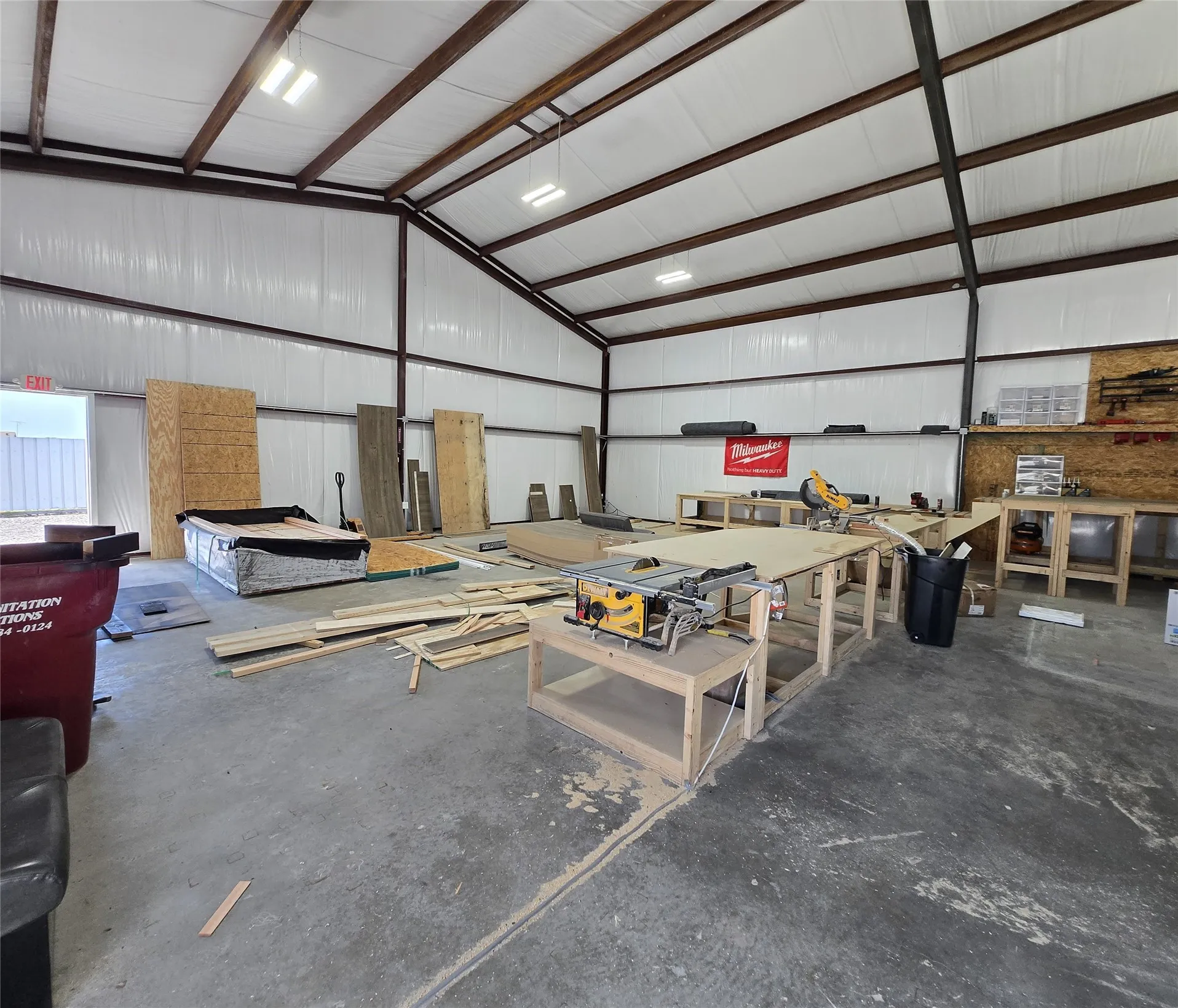 Spacious industrial interior featuring a vaulted ceiling with exposed metal beams, concrete flooring, white insulated walls, and overhead lighting