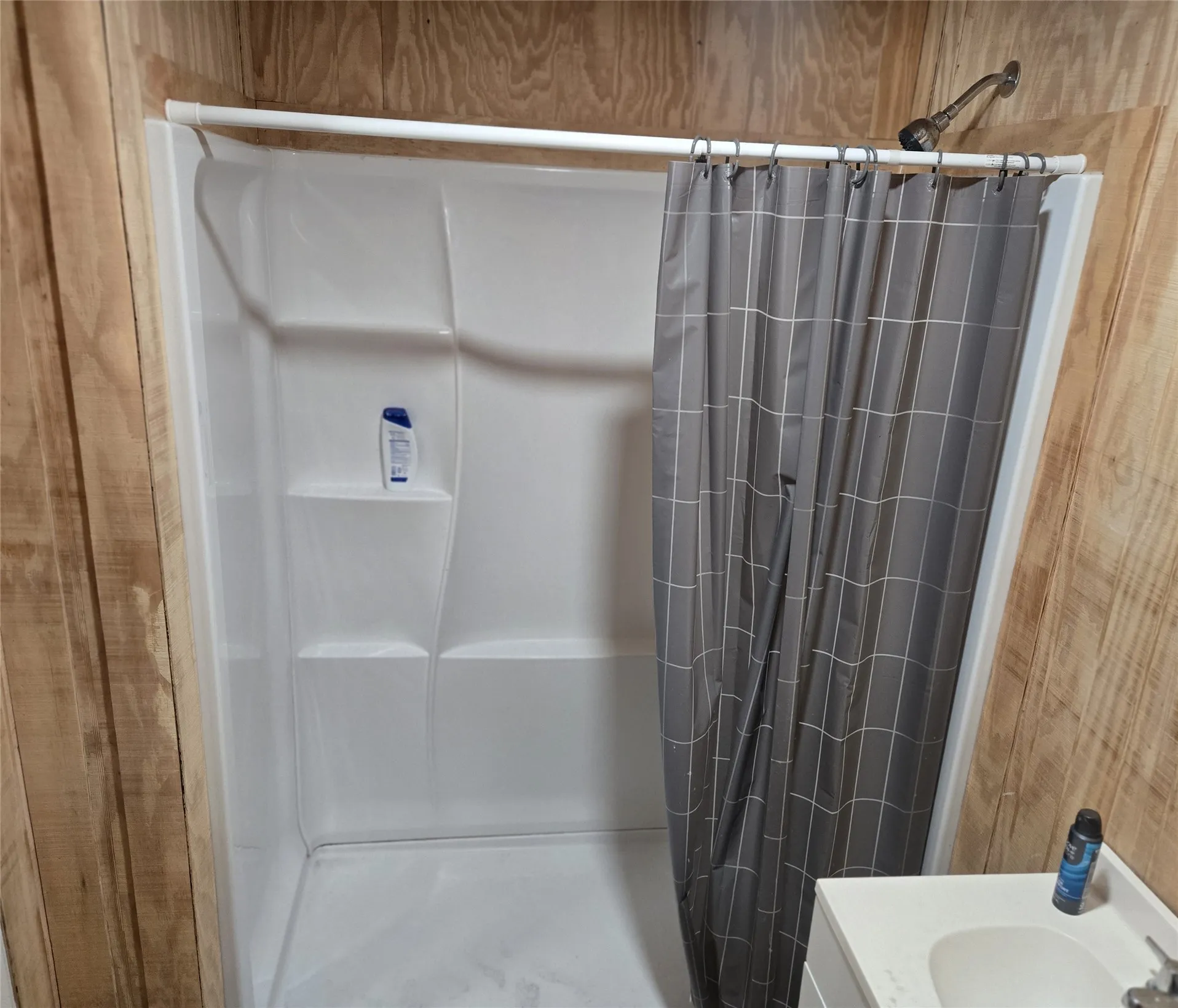 White shower stall featuring built-in shelving, a shower head, and a privacy curtain
