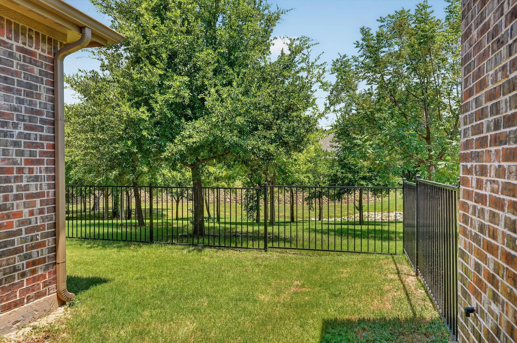 Expansive green lawn enclosed by a black metal fence, bordered by mature trees and brick exterior walls