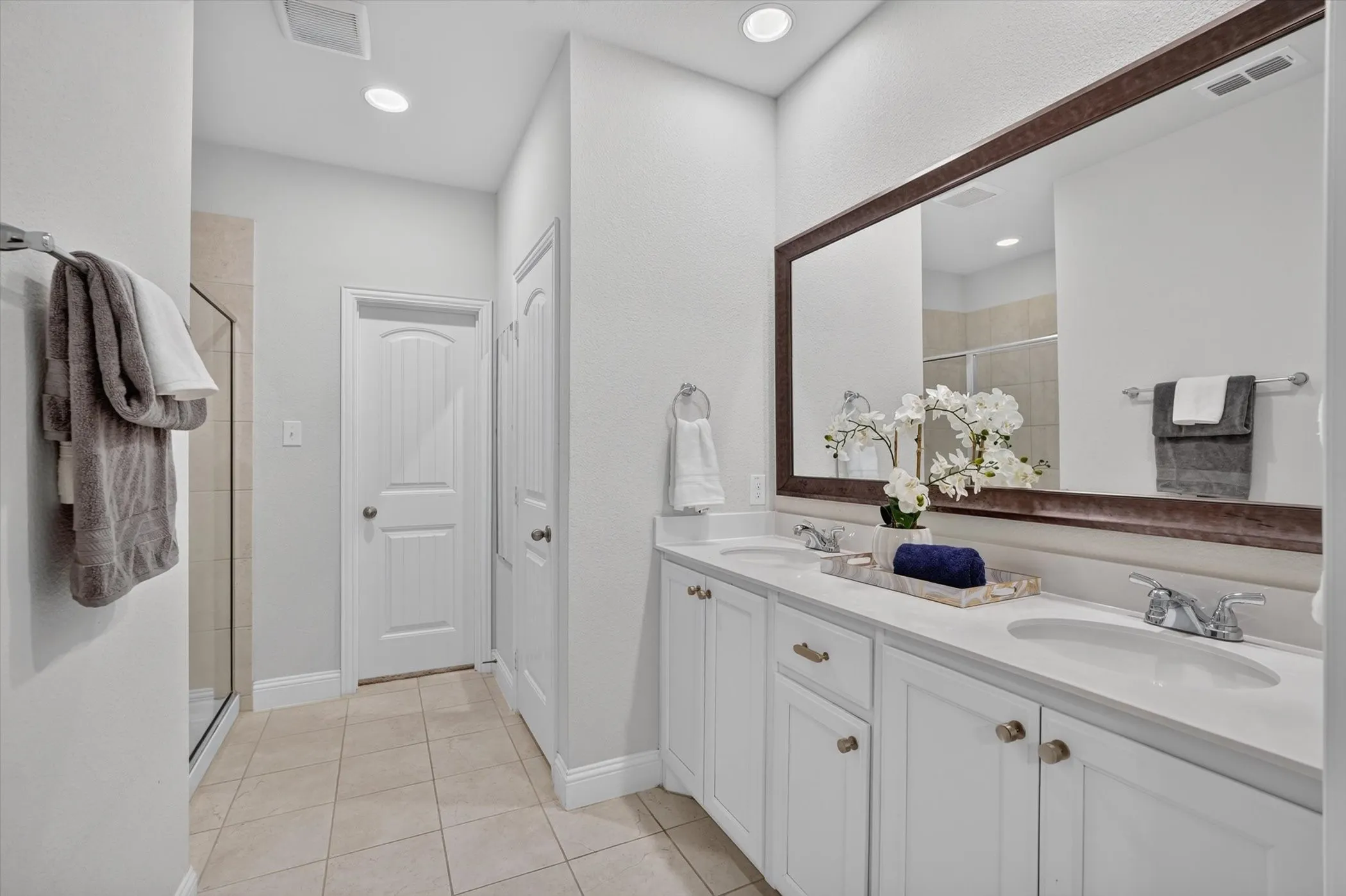 Dual vanity with white cabinetry, integrated sinks, chrome fixtures, and a large framed mirror