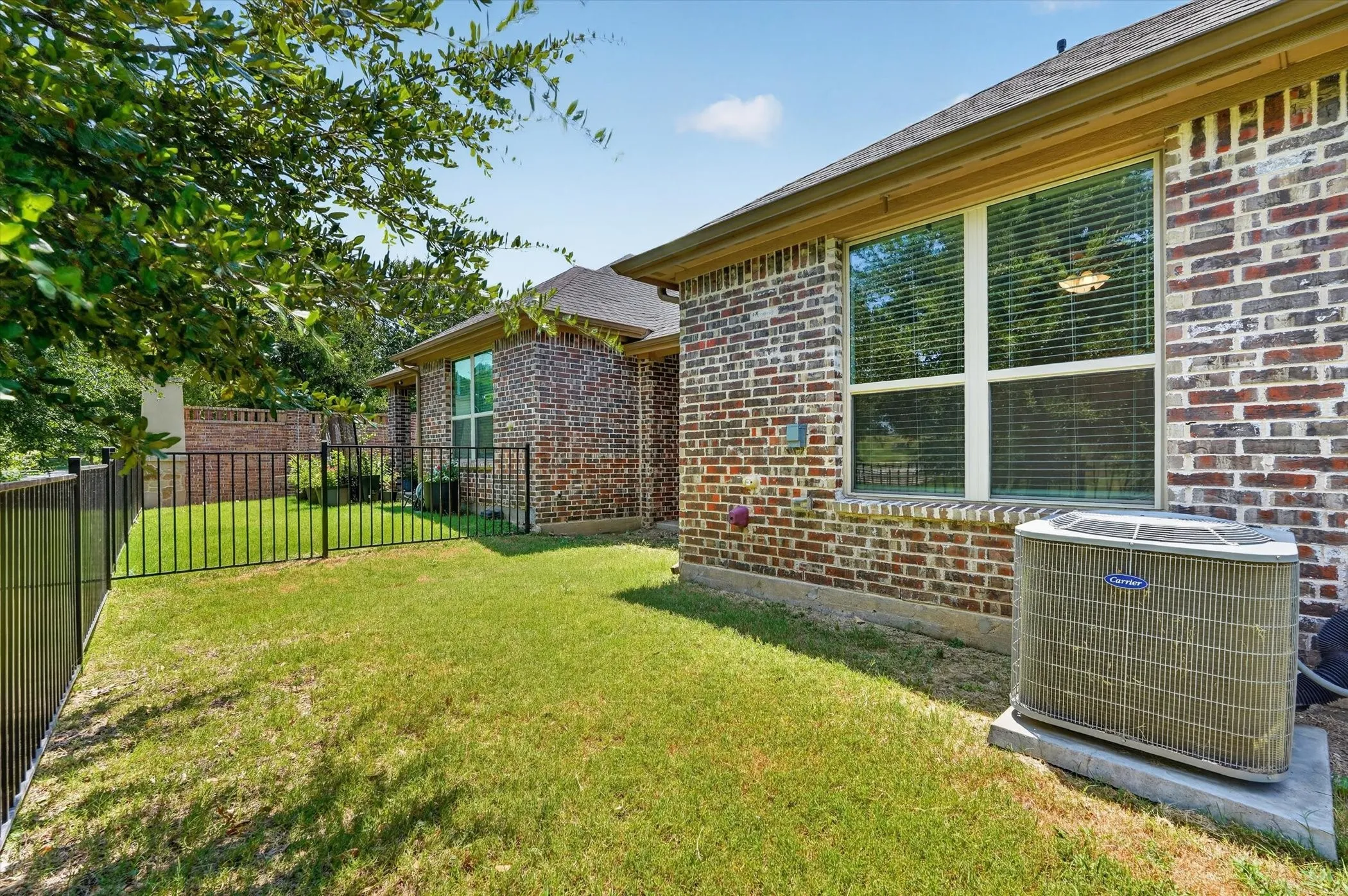 Rear exterior featuring a brick facade, white-framed window with blinds, and a private fenced yard with mature trees