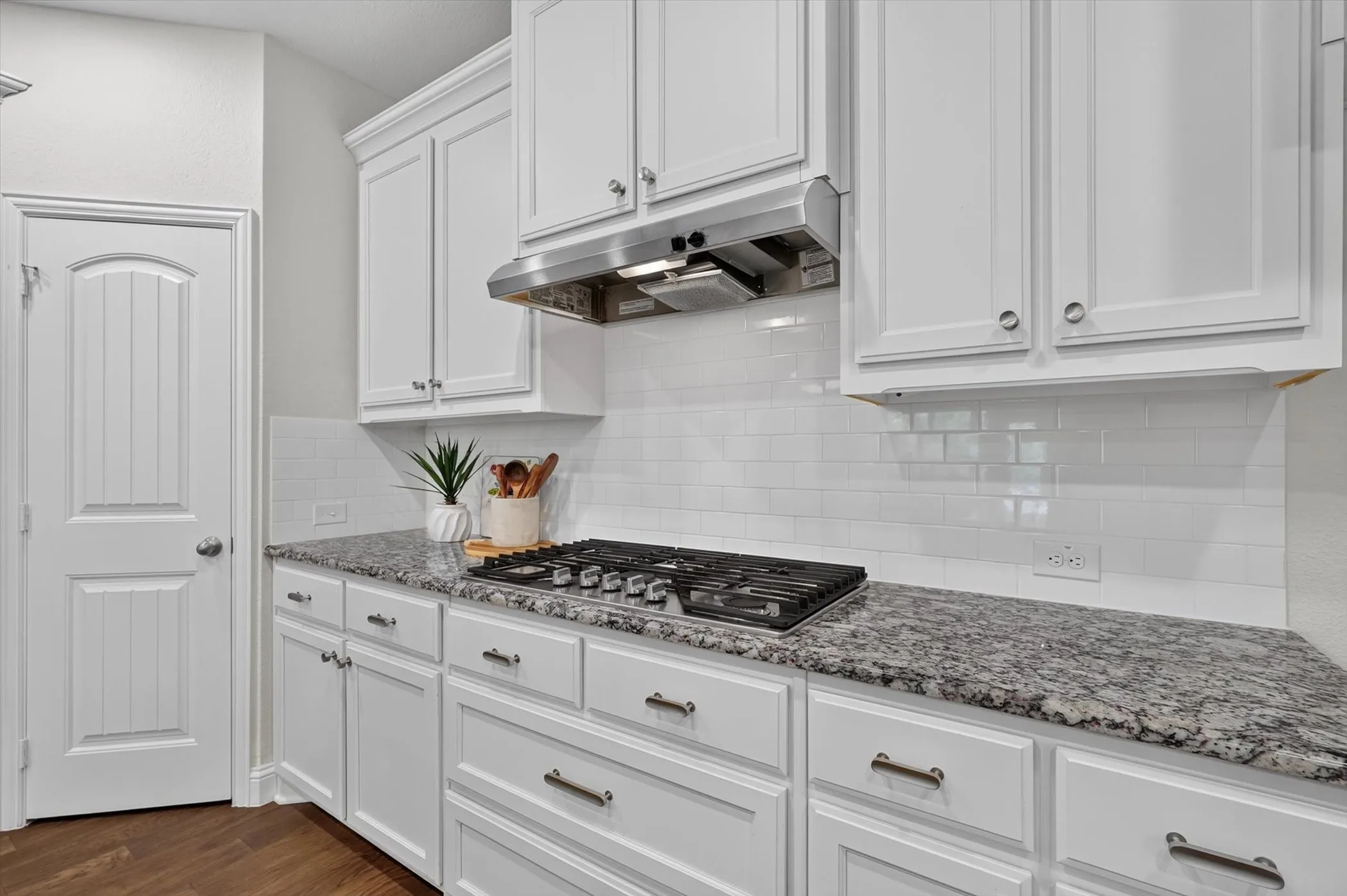 Kitchen featuring white shaker-style cabinetry, a gas cooktop with stainless steel vent hood, white subway tile backsplash, and granite countertops
