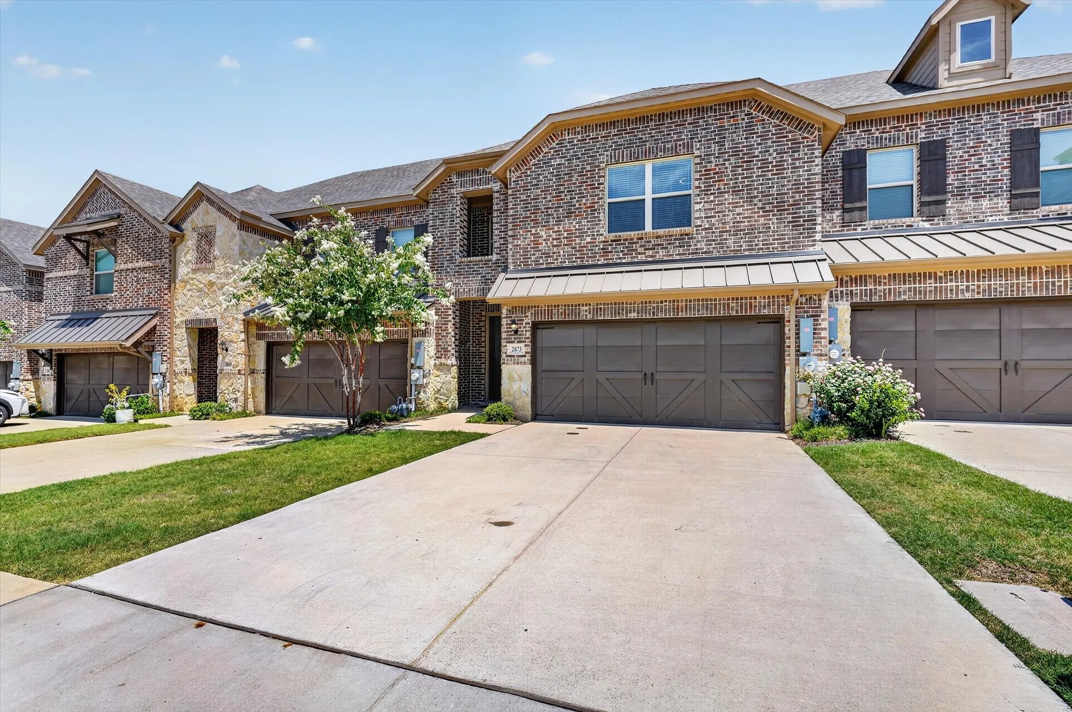 Brick and stone facade townhome featuring a two-car garage with decorative doors and a metal​​‌​​​​‌​​‌‌​‌‌​​​‌‌​‌​‌​‌​​​‌​​ awning