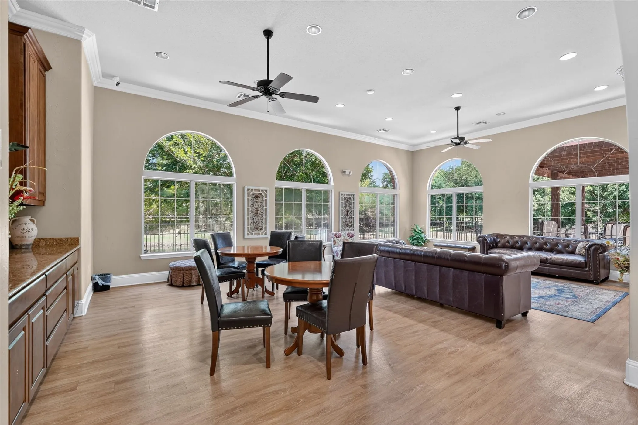 Spacious communal area featuring extensive arched windows, wood-finish flooring, recessed lighting, and ceiling fans