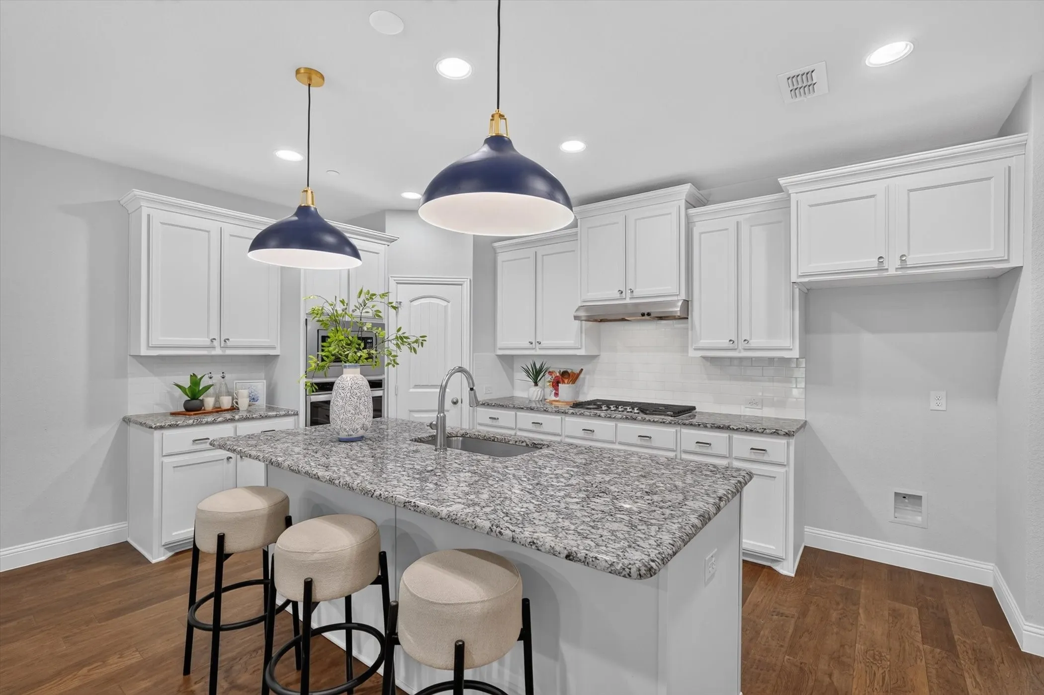 Spacious kitchen featuring an expansive center island with granite countertop, white shaker cabinetry, stainless steel appliances, and wood-finish flooring