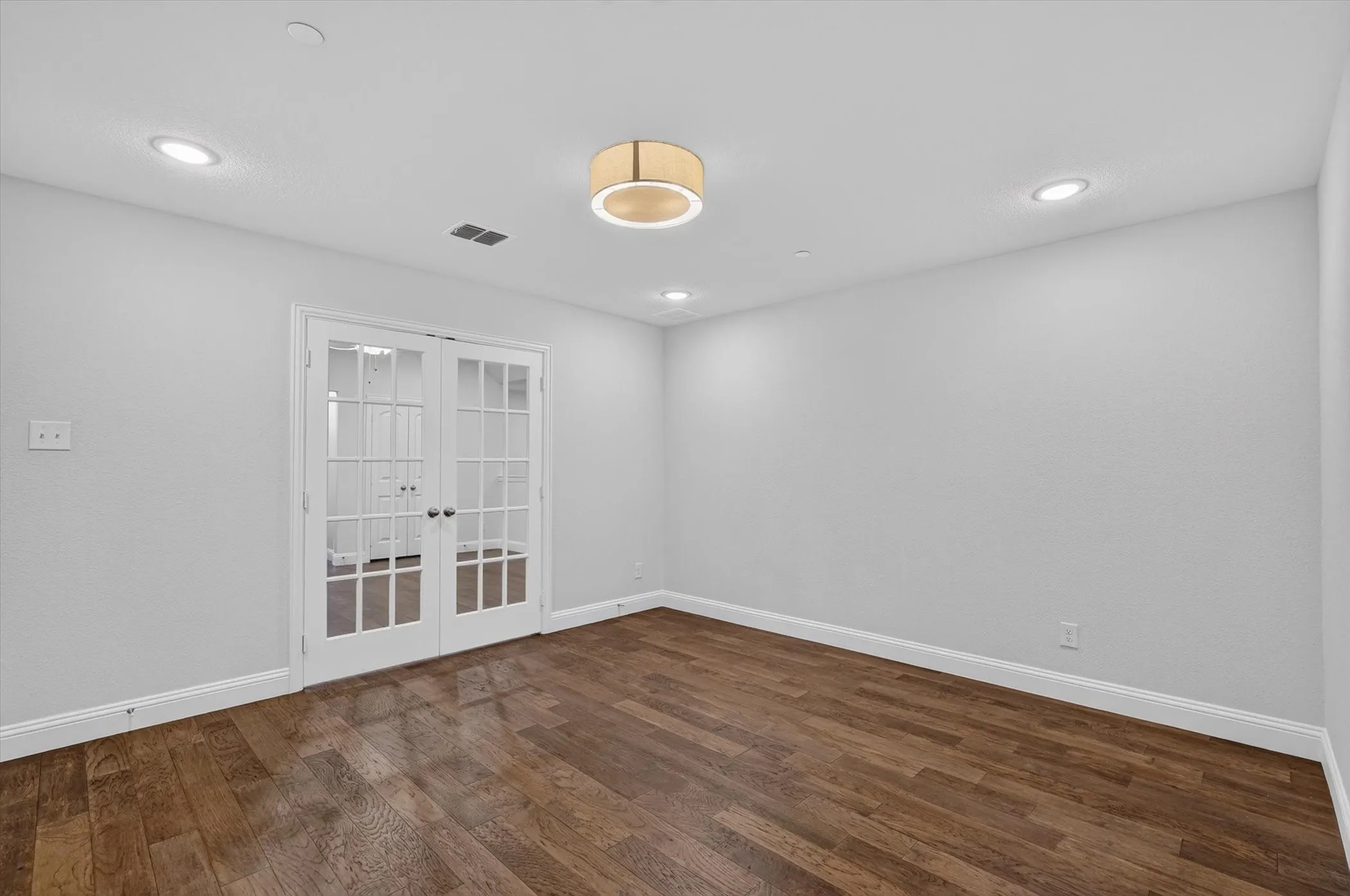 Spacious room featuring wood-finish flooring, white baseboards, and light gray walls