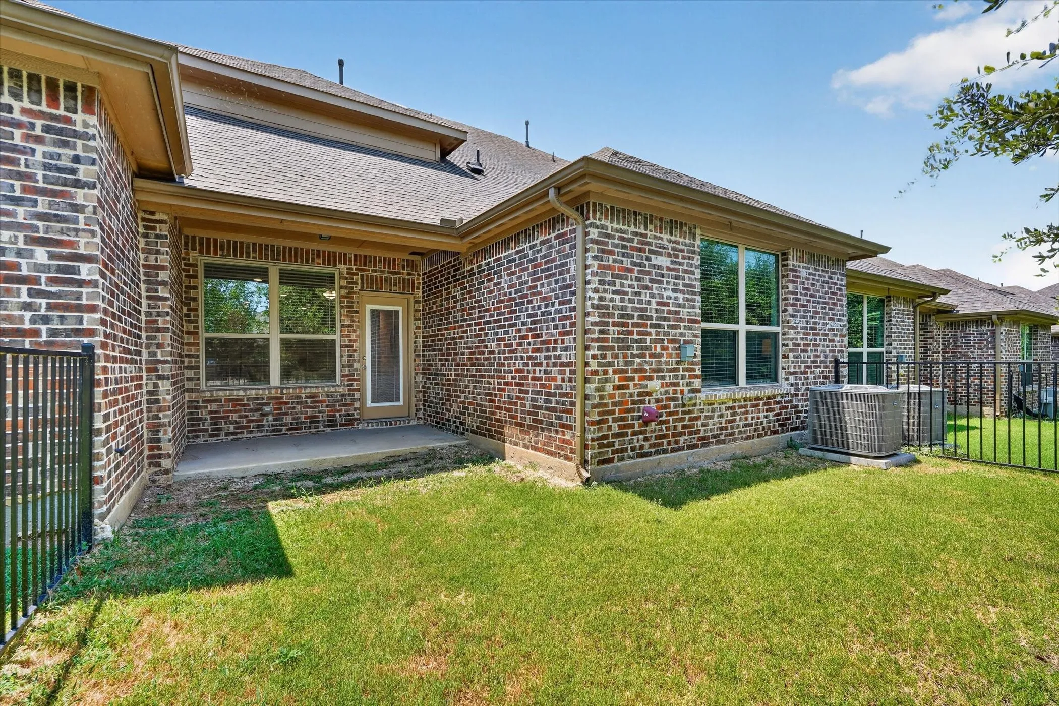 Brick exterior featuring a covered concrete patio, an exterior door with a screen, and multiple windows