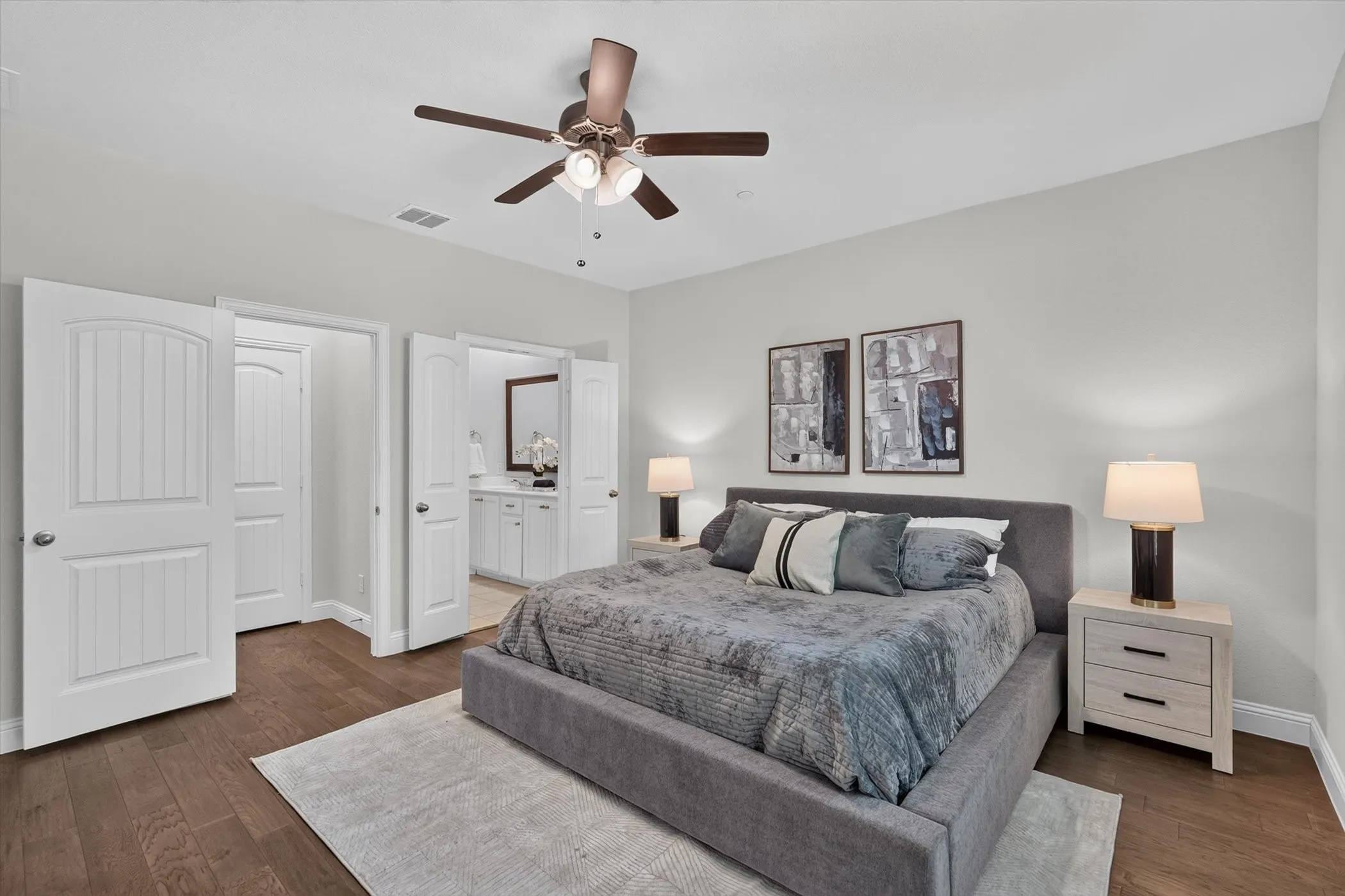 Spacious bedroom featuring wood-finish flooring, light grey walls, and a ceiling fan with integrated lighting