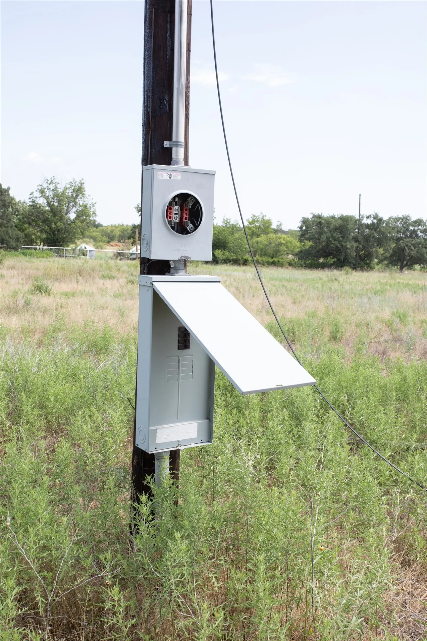 Utility pole with a mounted electrical meter base and a gray panel box with an open door