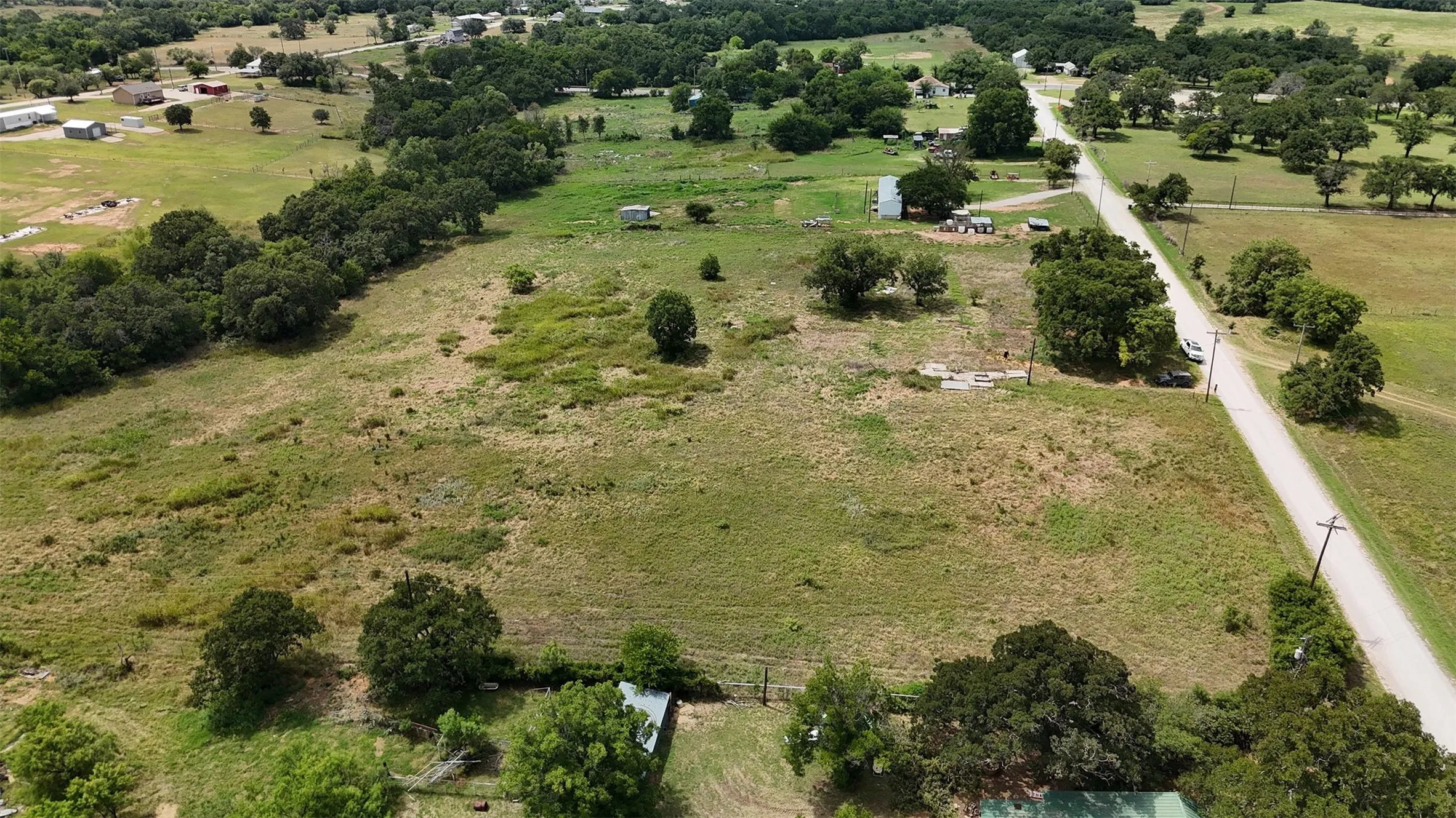 Expansive land parcel featuring a gravel road, scattered mature trees, and a mix of grassy and cleared areas
