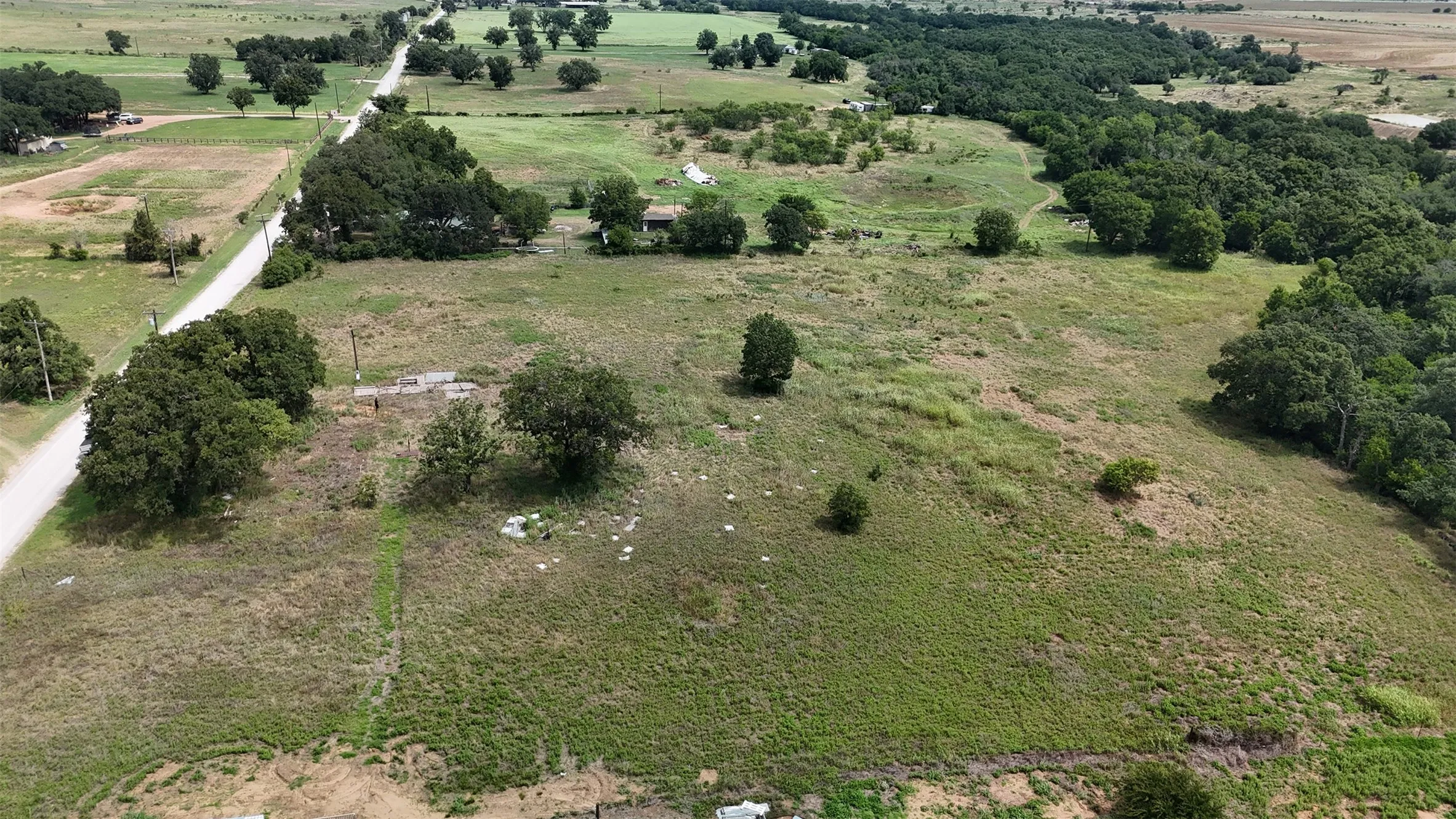 Expansive land parcel featuring a tree-lined perimeter, a partially paved road, and varied topography