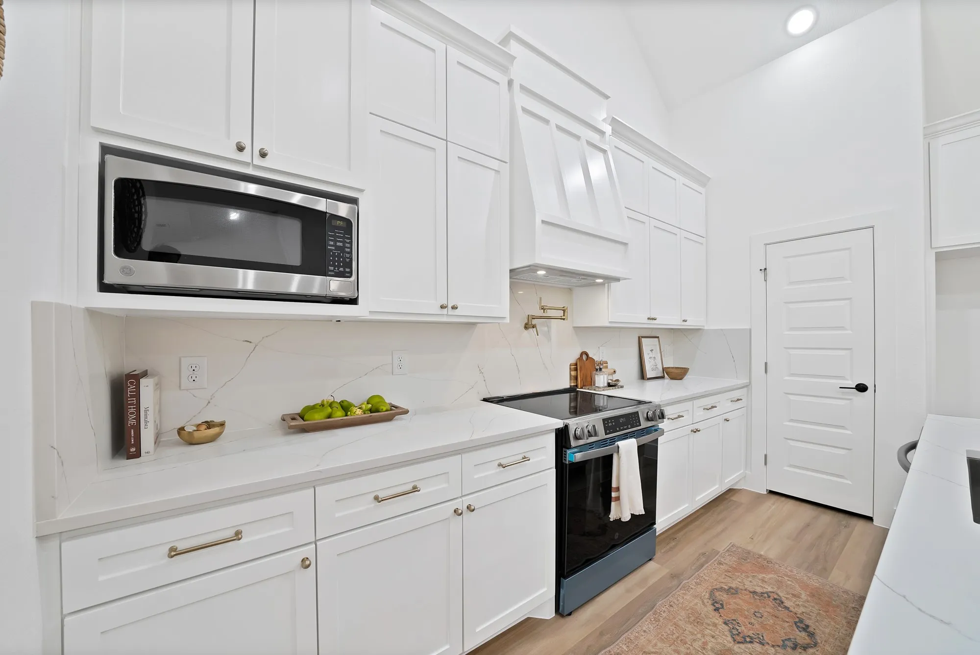 Bright kitchen featuring white cabinetry, integrated stainless steel microwave, stone countertops with veining, and wood-finish flooring