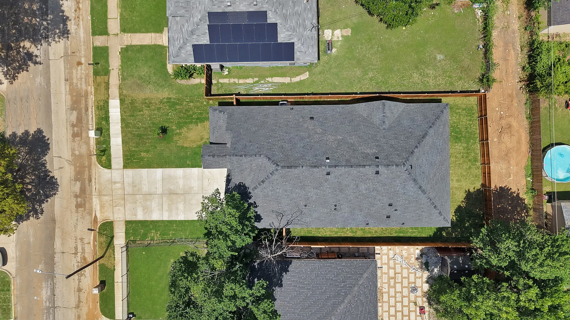 Gable roof home featuring a dark shingle roof, a concrete driveway, a front lawn, and a fenced backyard