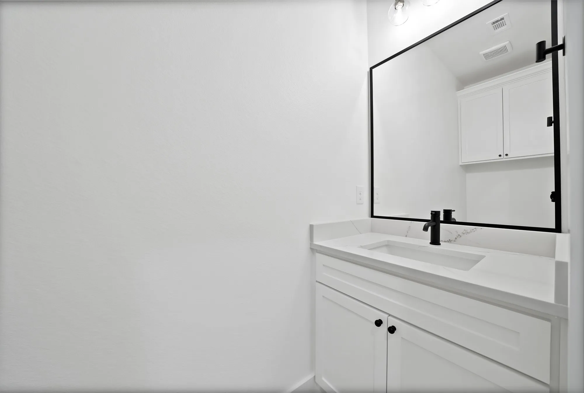 White shaker-style vanity with matte black hardware, integrated rectangular sink, and quartz countertop