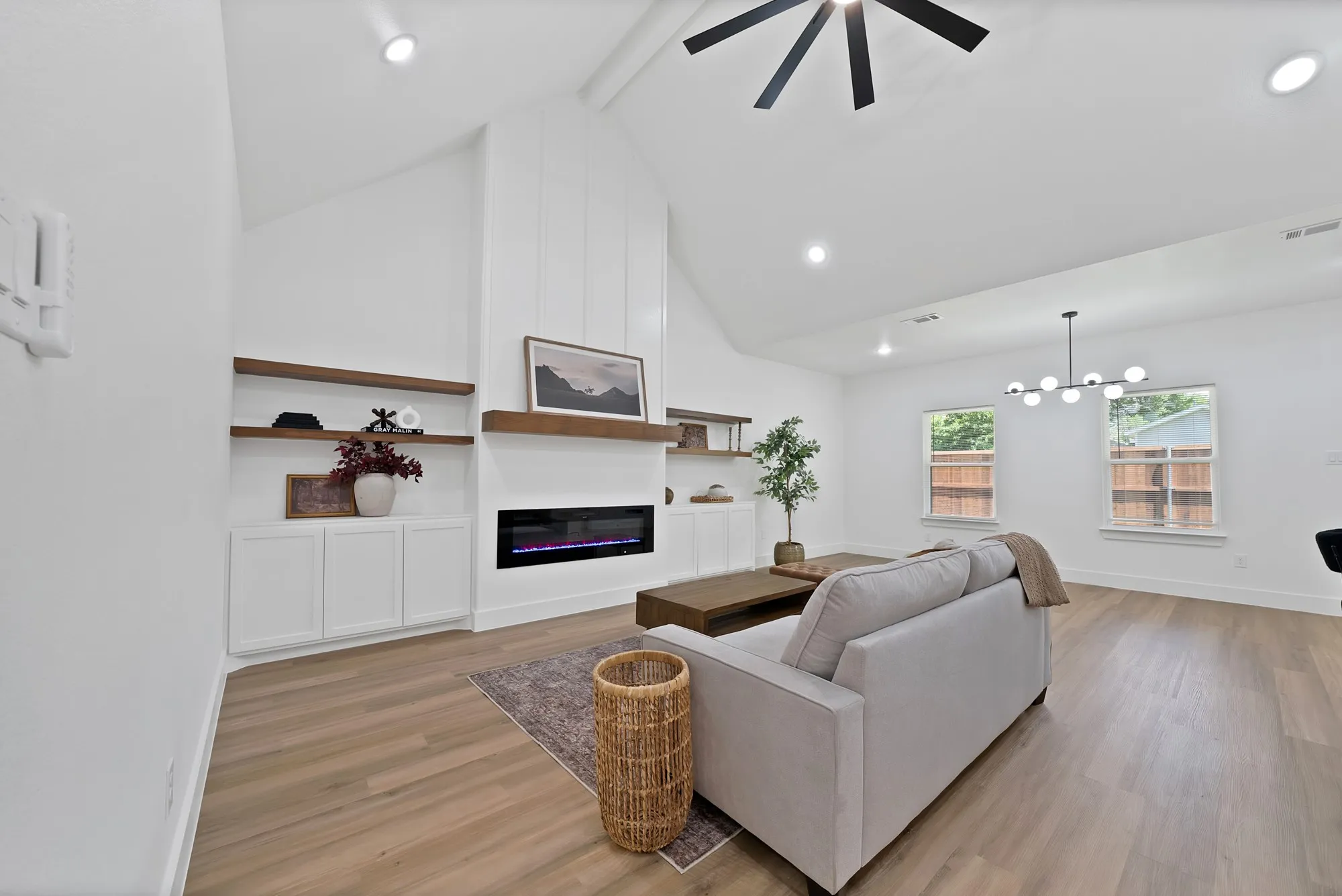 Spacious living area featuring a vaulted ceiling with recessed lighting and a ceiling fan, a contemporary linear electric fireplace, wood-finish flooring, and built-in shelving with lower cabinetry