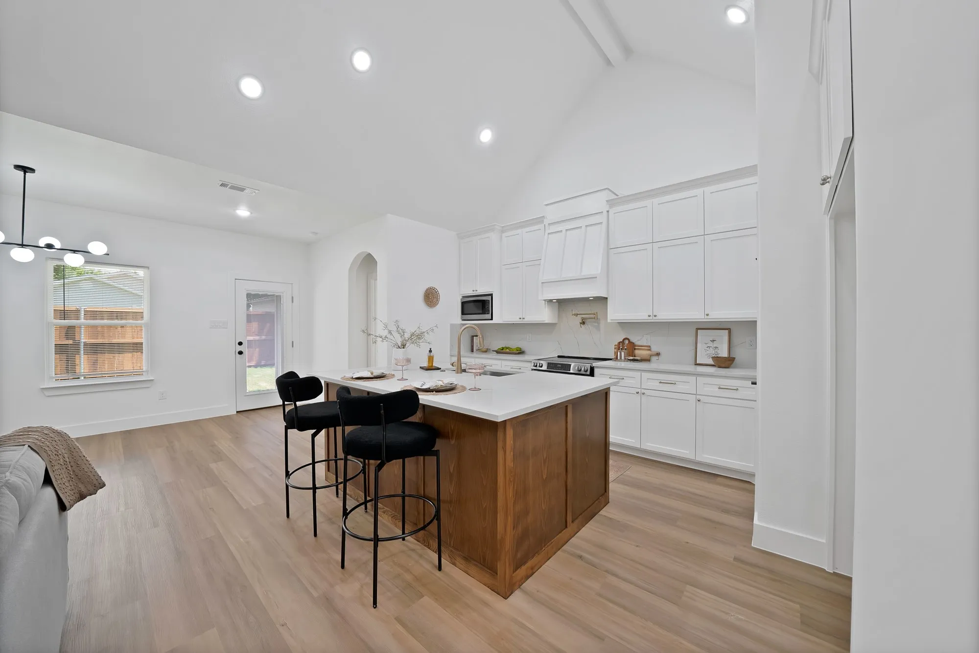 Vaulted ceiling kitchen featuring a central island with countertop seating, wood-finish flooring, white cabinetry, and recessed lighting