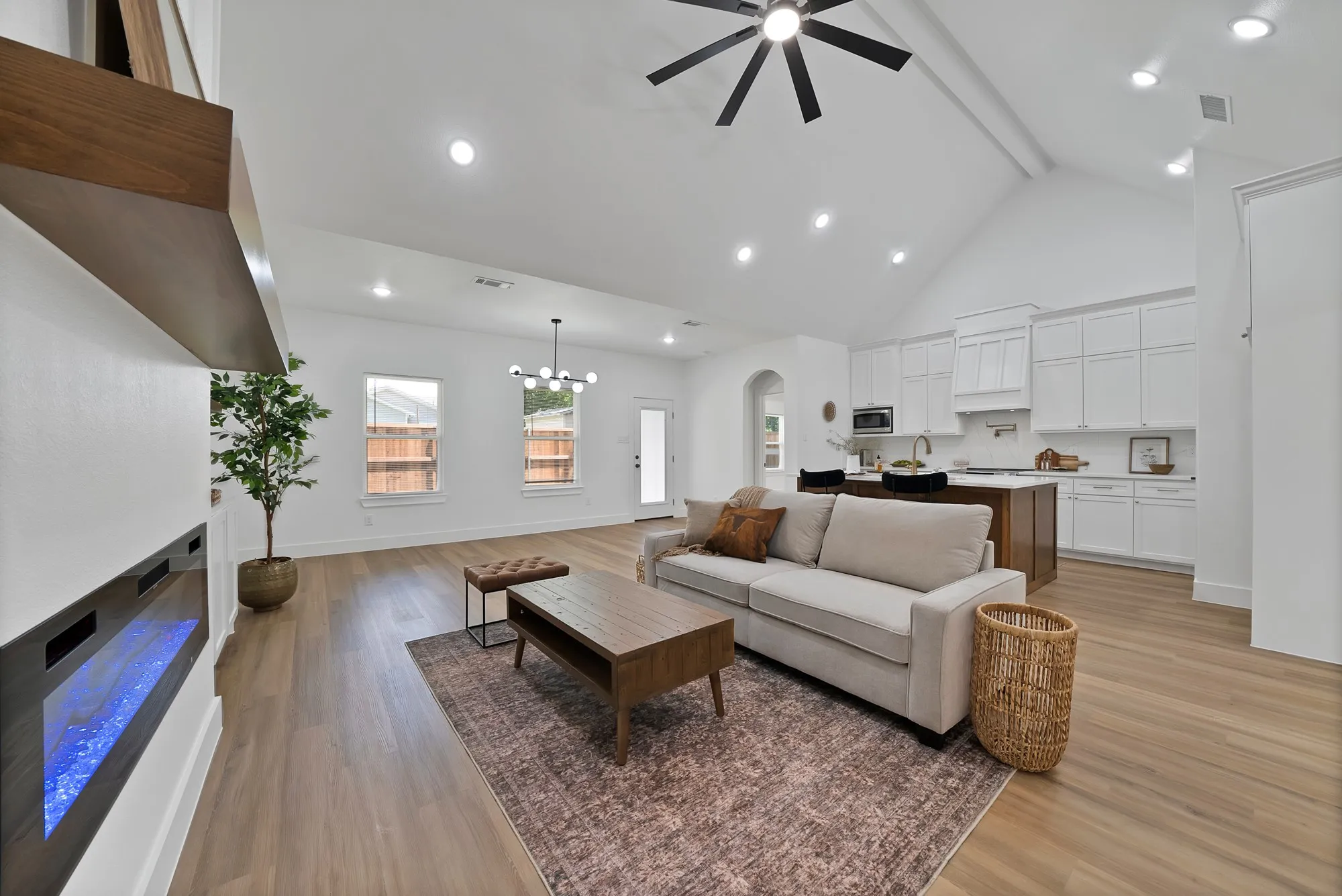 Open-concept living space featuring vaulted ceilings, wood-finish flooring, a contemporary electric fireplace, recessed lighting, and a modern kitchen with white cabinetry and a wood-tone island