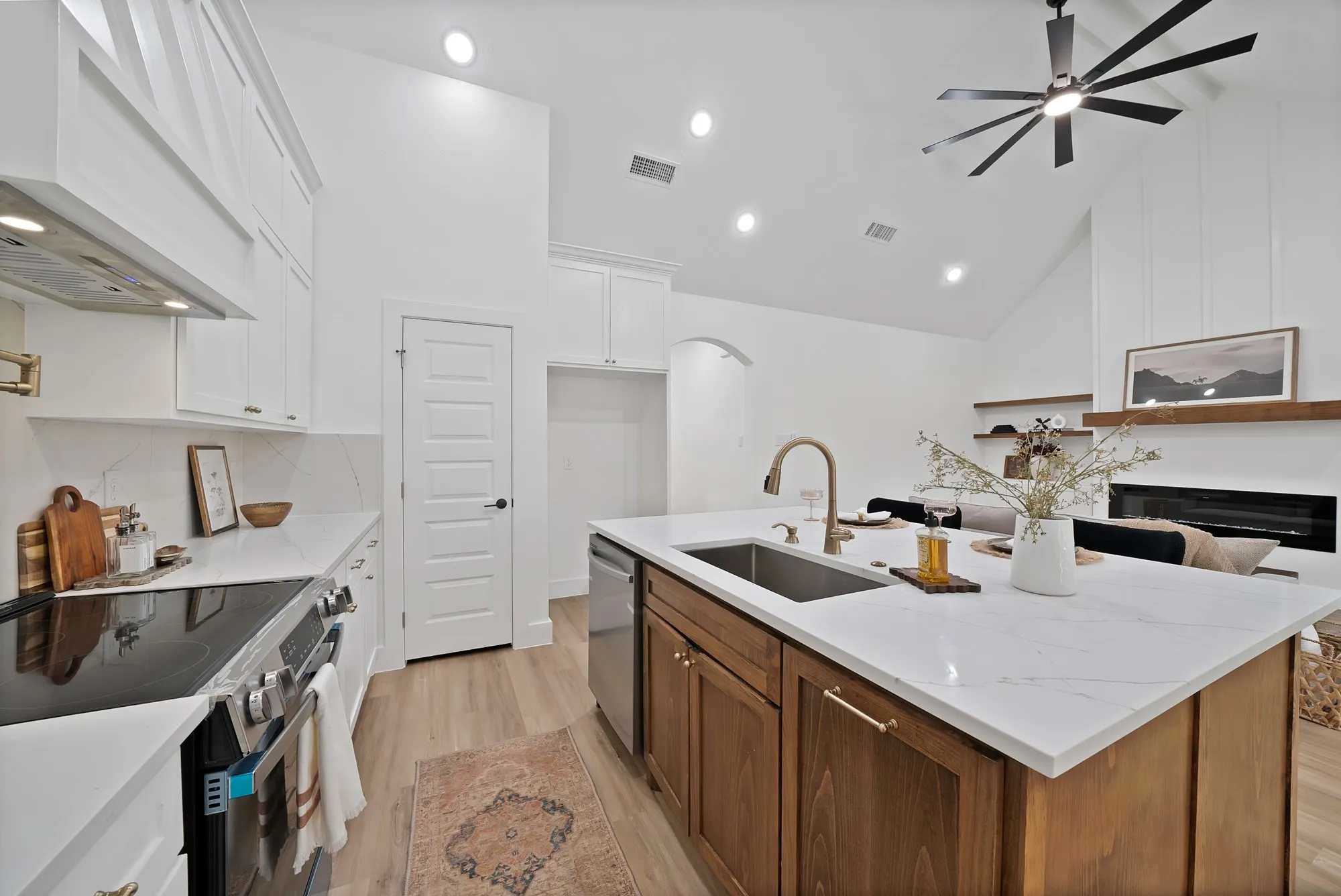 Open-concept kitchen featuring an island with a stainless steel undermount sink, a gold-tone faucet, and white countertops