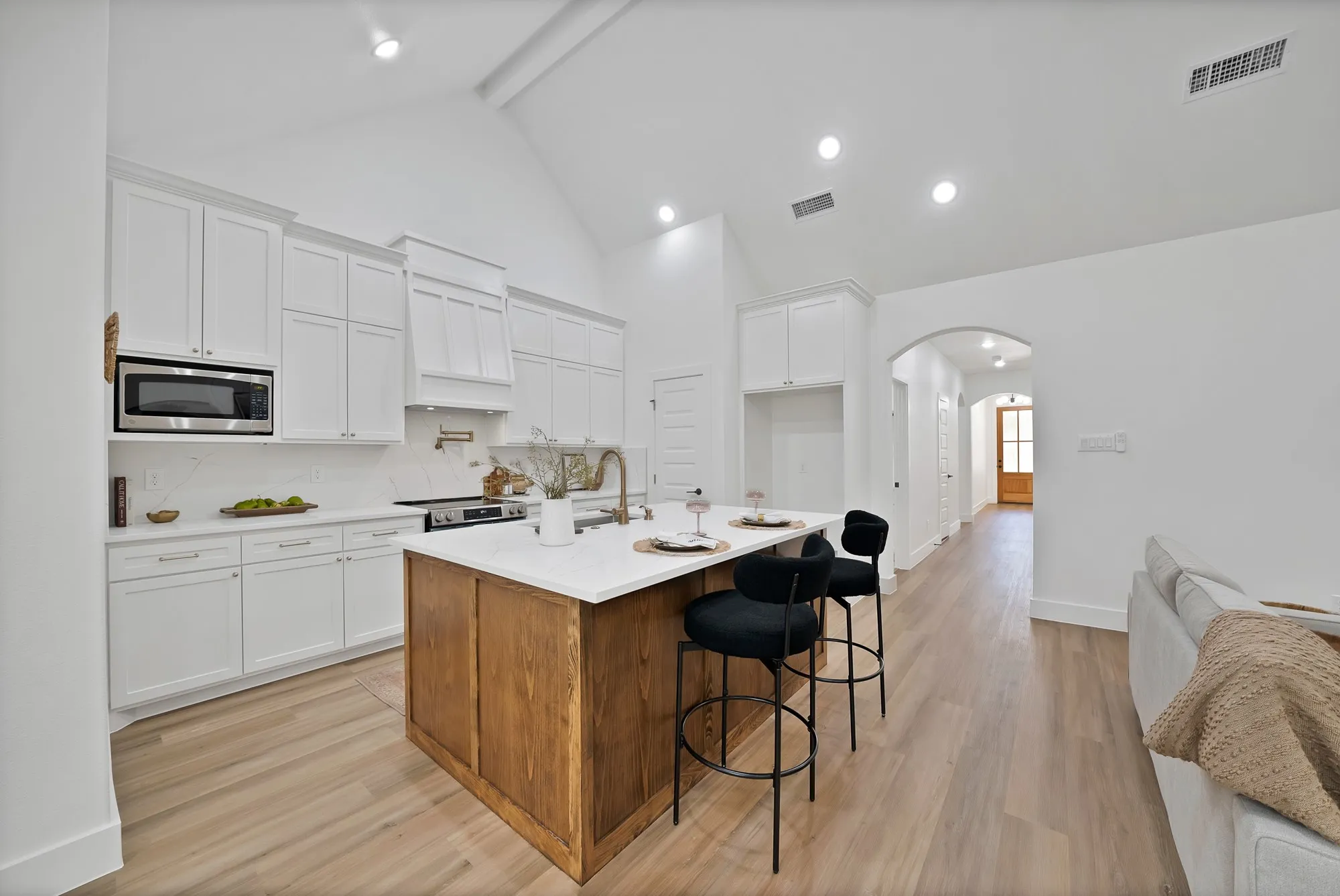 Open-concept kitchen featuring a vaulted ceiling with recessed lighting, a wood-finish island with a light-toned countertop, white cabinetry, a stainless steel microwave, and wood-finish flooring