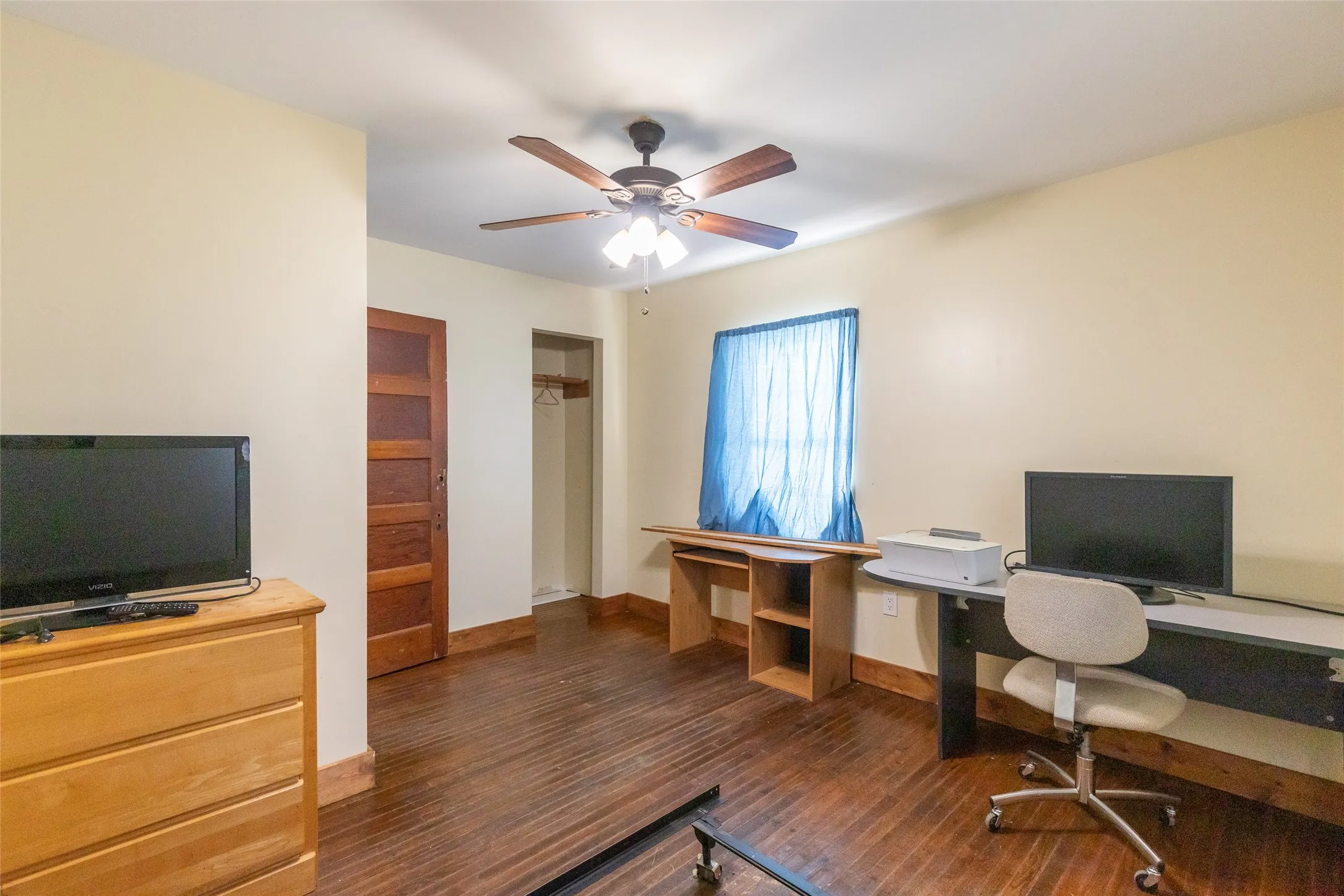 Interior room with wood-finish flooring, a ceiling fan with integrated lighting, and a window with blue curtains