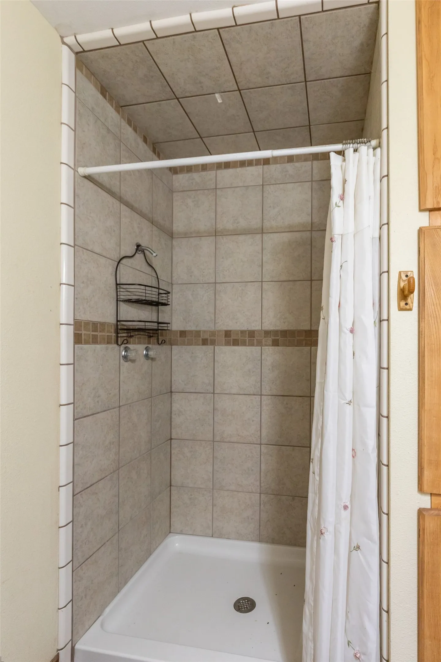 Shower stall featuring a white base, neutral-toned wall tiling, and a contrasting mosaic tile accent band