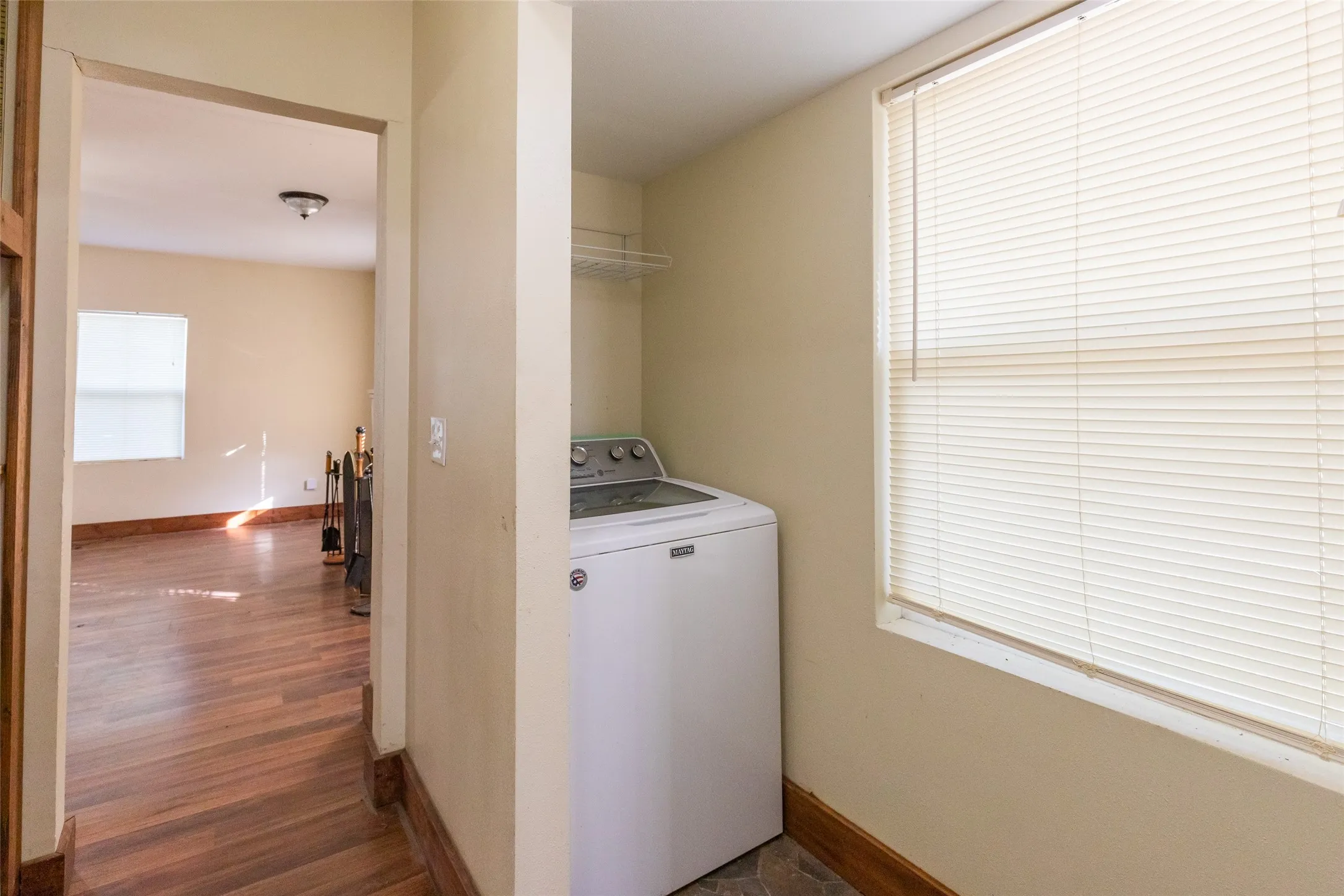 Dedicated laundry area featuring a top-load washer, overhead wire shelving, and a window with blinds