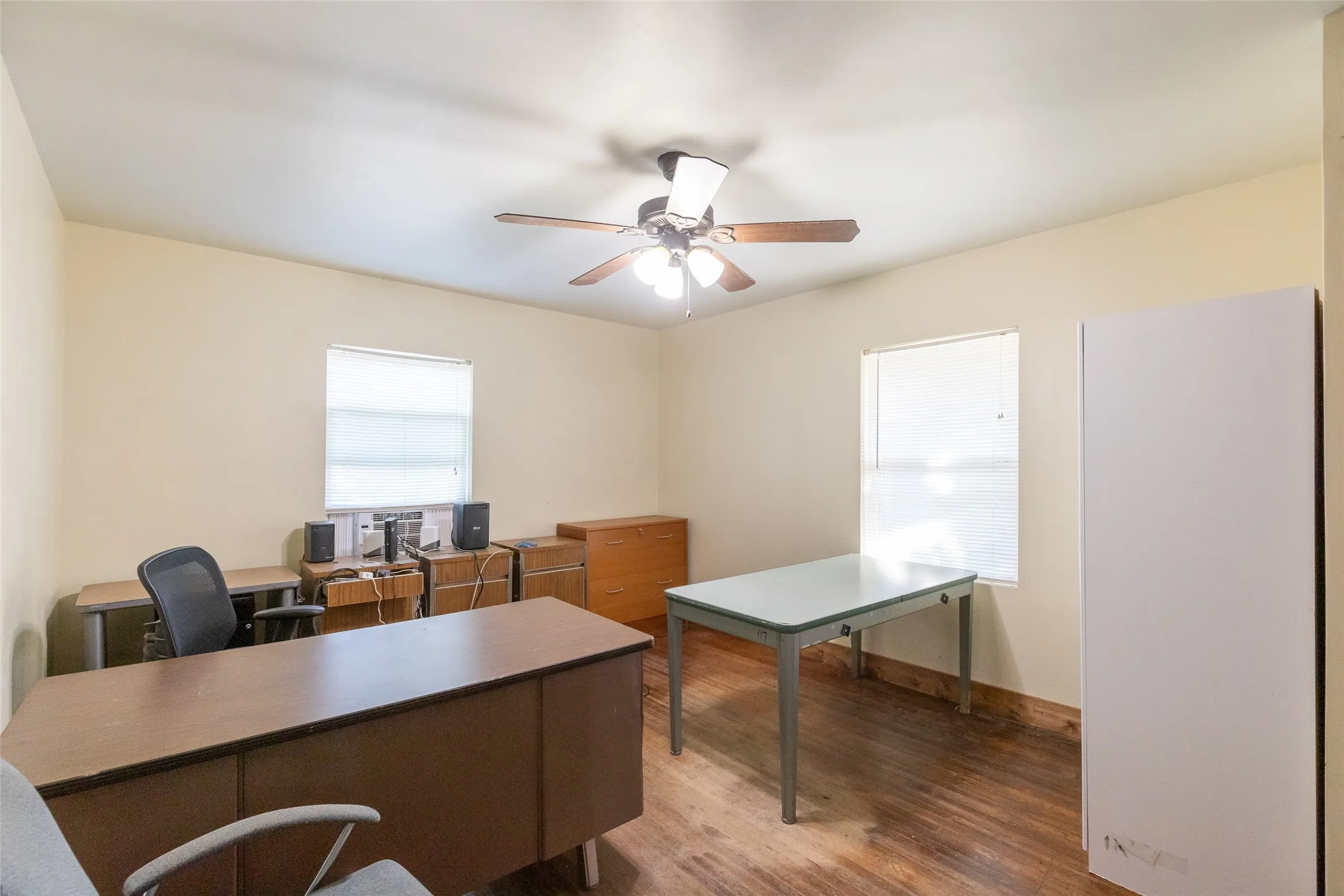 Spacious room featuring wood-finish flooring, two windows, and a ceiling fan with integrated lighting