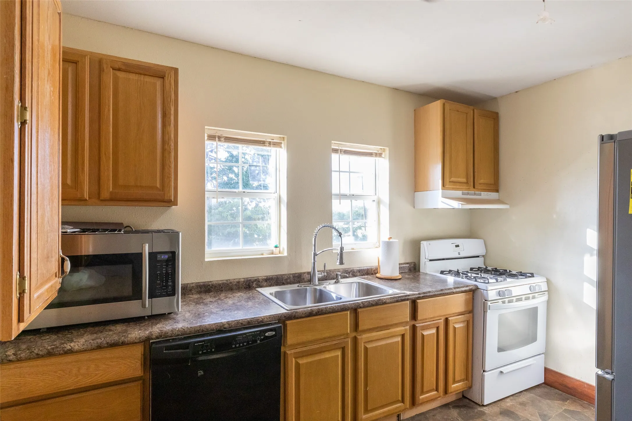Kitchen featuring wood cabinetry, laminate countertops, dual basin stainless steel sink, and a white gas range