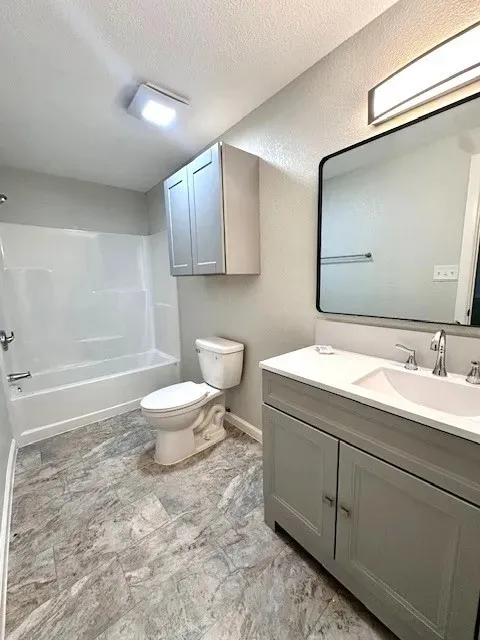 Full bathroom featuring a single vanity with a white countertop and undermount sink, a framed mirror, a tub/shower combination, and patterned flooring