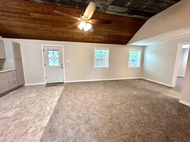 Open concept living area featuring a wood-panel ceiling with a ceiling fan, light gray painted walls, and an entryway with a decorative glass door
