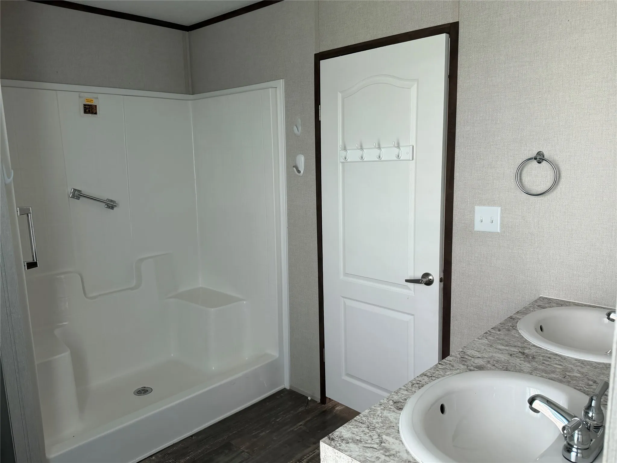 Bathroom featuring a white shower stall with built-in seating, dual vanity sinks, wood-finish flooring, and light-toned wall finishes