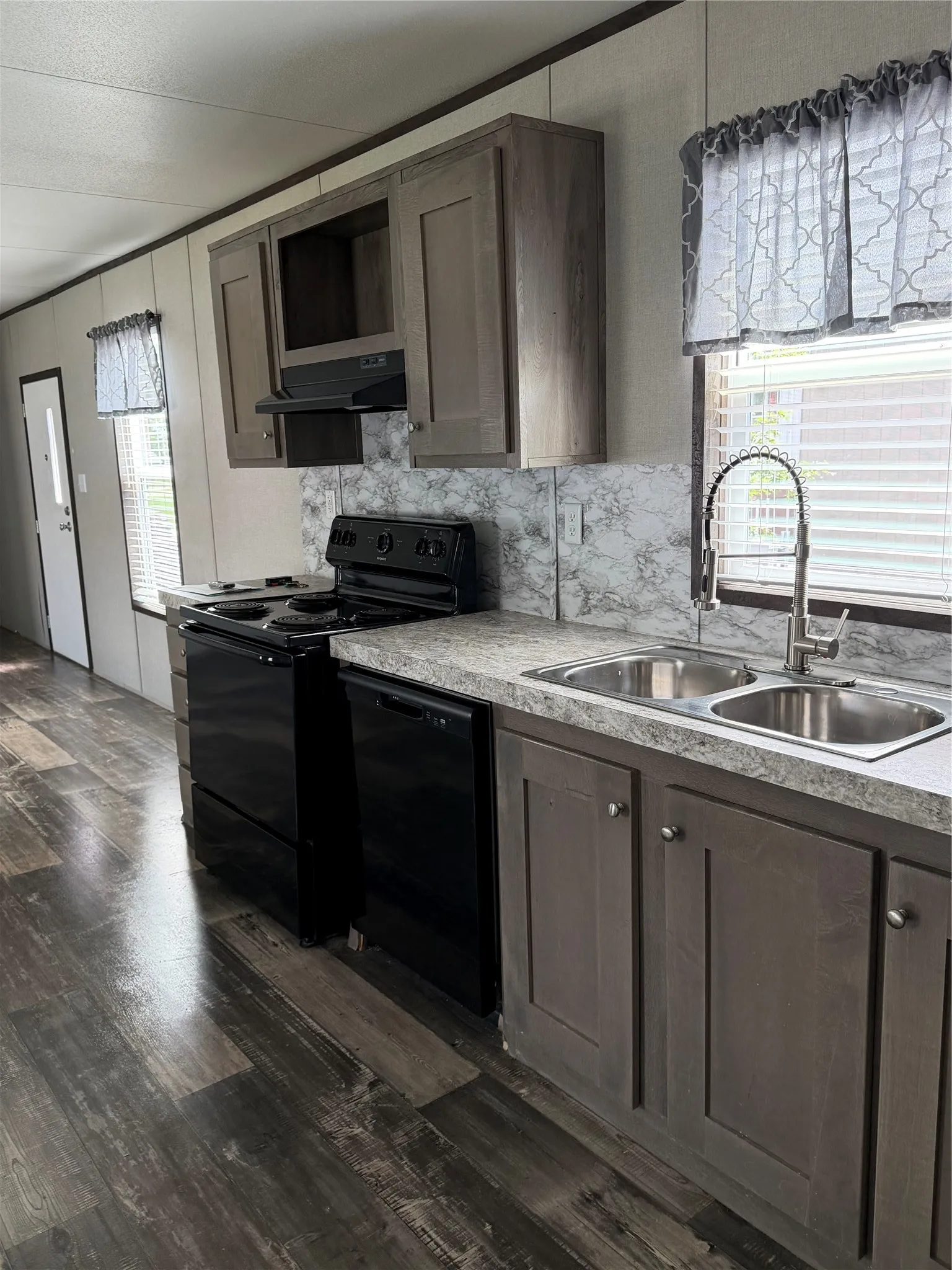 Kitchen featuring dark wood-finish flooring, two-tone cabinetry with upper and lower storage, black electric range, black dishwasher, and double basin stainless steel sink with gooseneck faucet