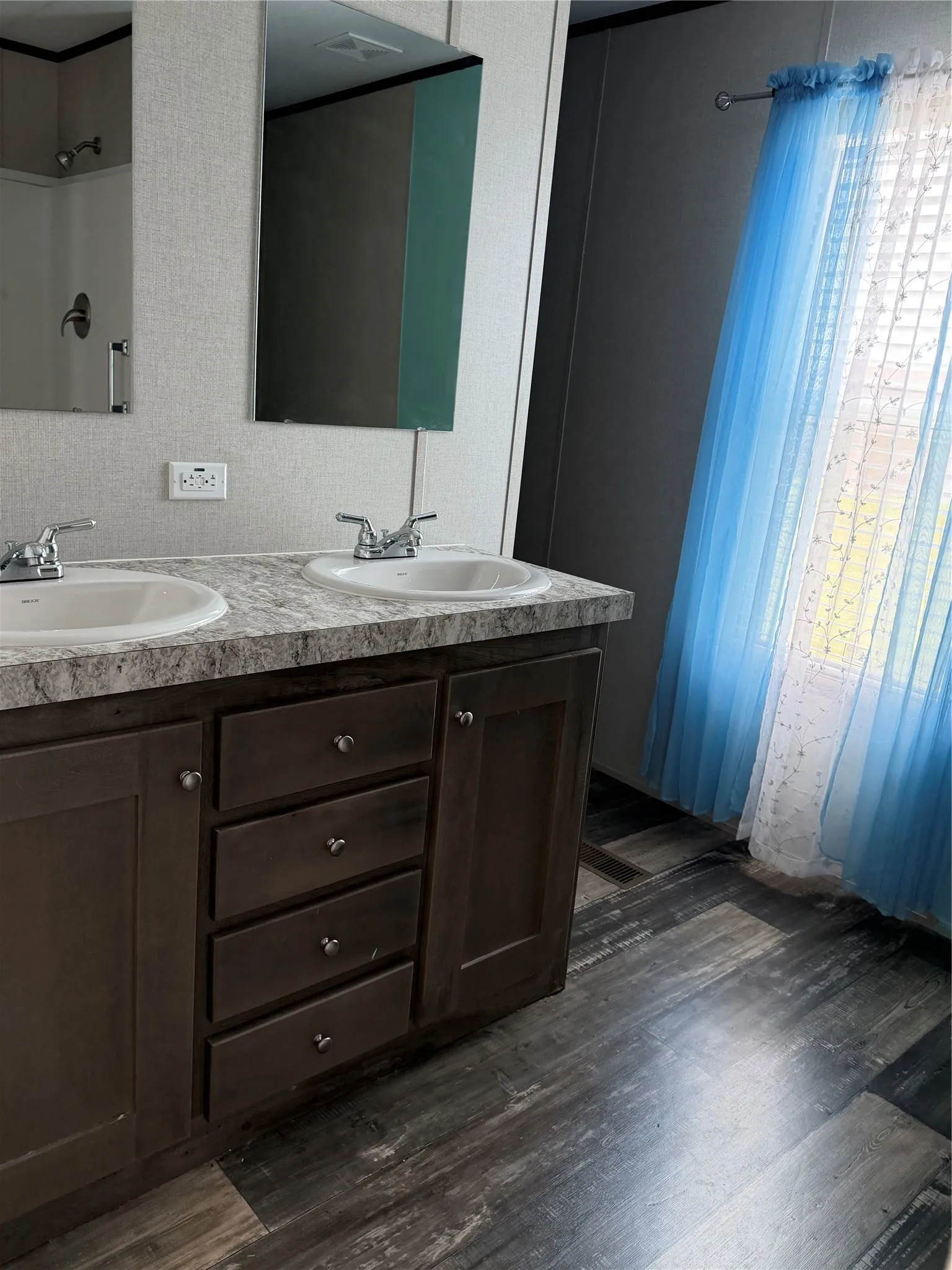Bathroom vanity featuring dual sinks with individual faucets, a speckled countertop, and dark wood-finish cabinetry