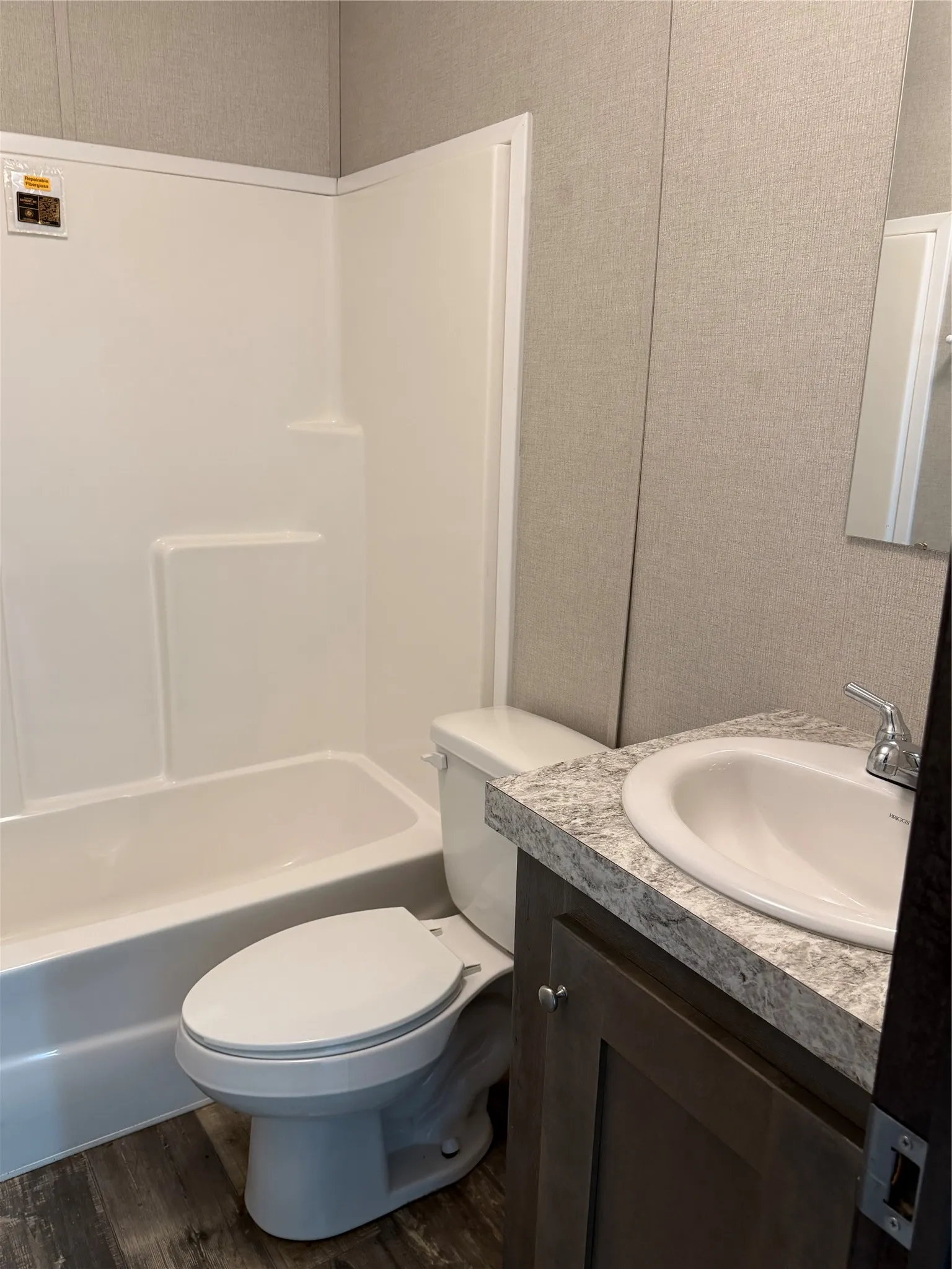Full bathroom featuring a white tub/shower combination, white toilet, and a vanity with a white basin sink, laminate countertop, and wood-finish cabinetry