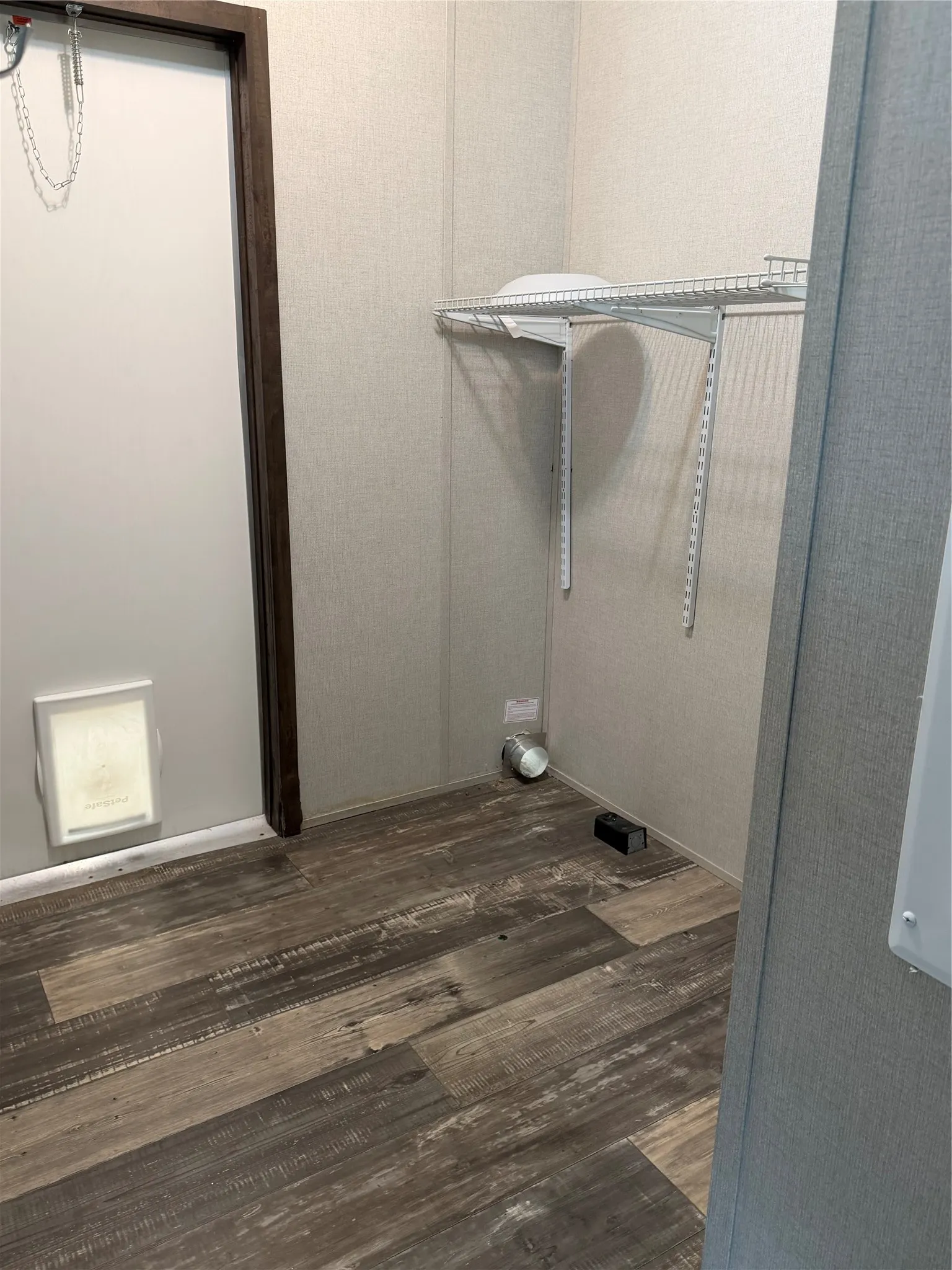 Dedicated utility area featuring wood-finish flooring, textured wall panels, and a wall-mounted wire shelving system