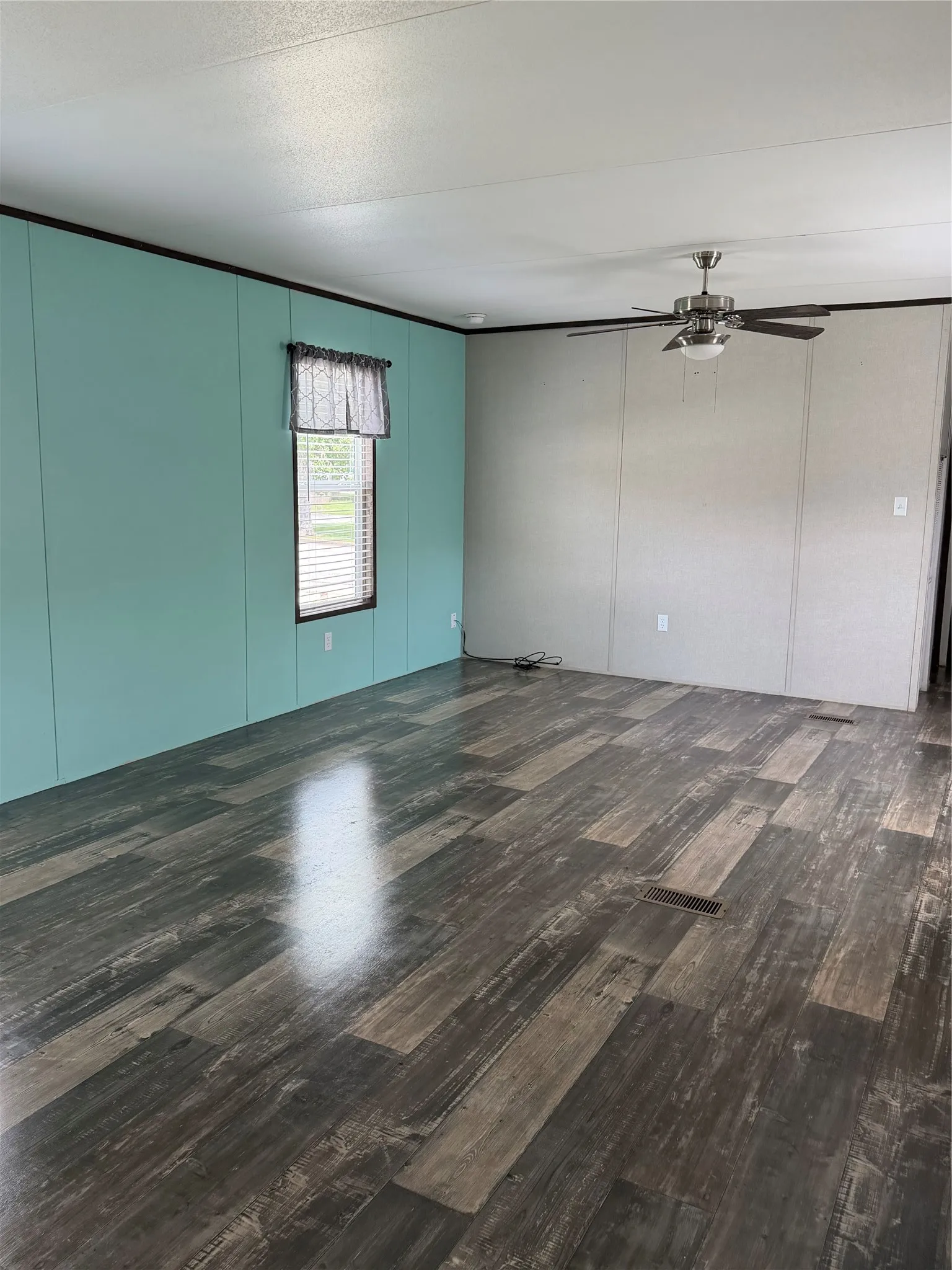 Spacious interior featuring wood-finish flooring, a ceiling fan with integrated lighting, and a window with blinds