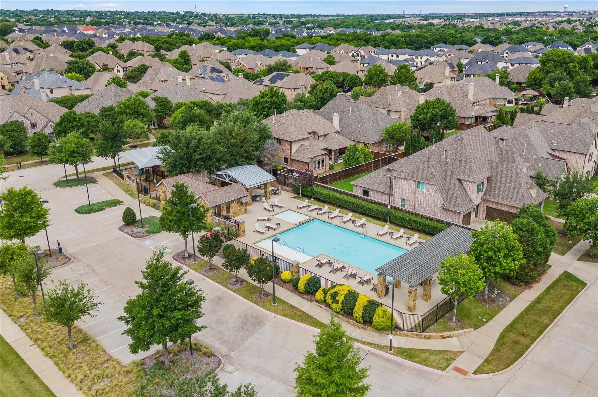 Community swimming pool with surrounding lounge areas, stone-clad pavilion structures, and a dedicated parking area