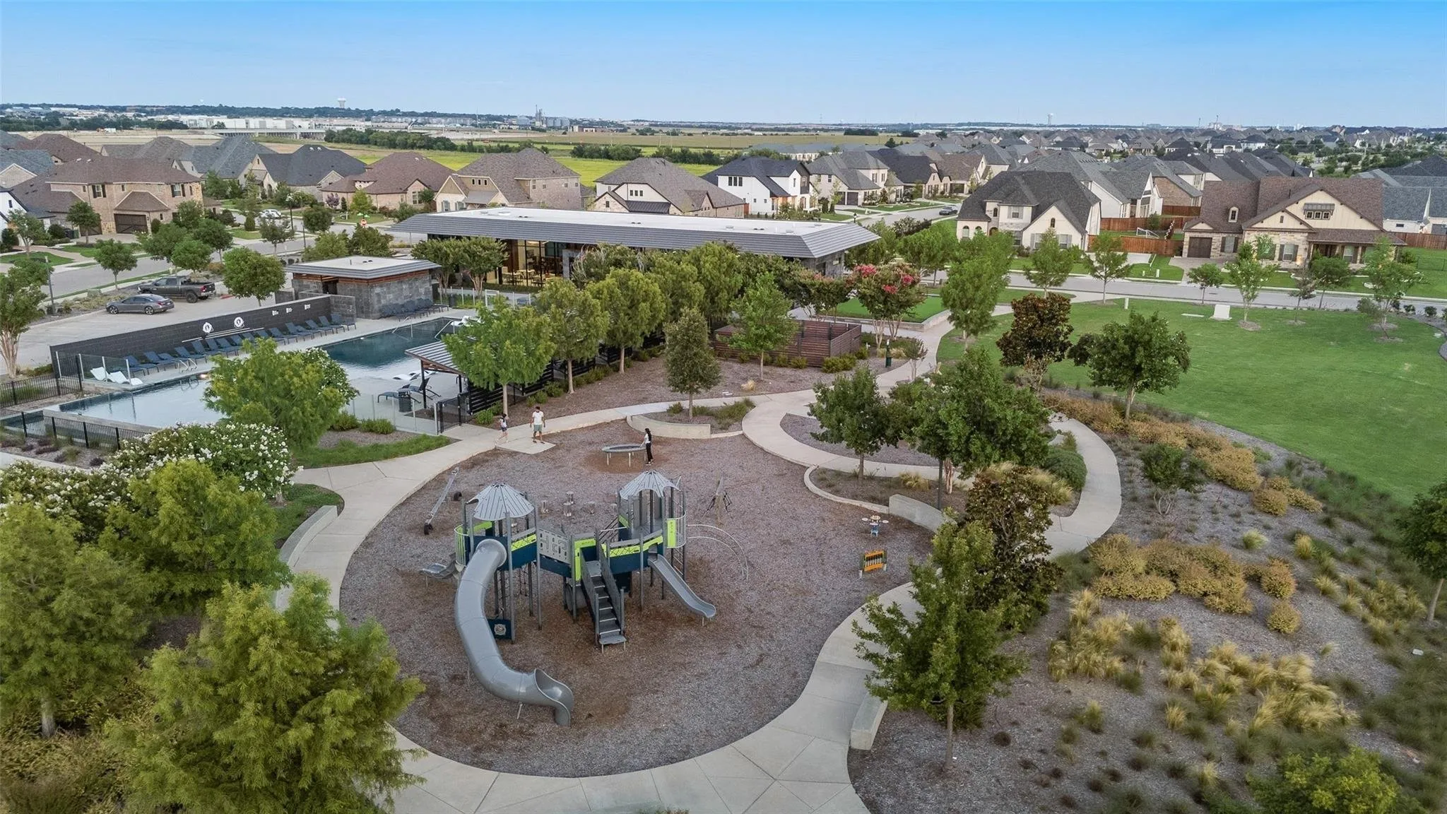 Community green space featuring a playground with slides, a swimming pool with lounge seating, and a clubhouse building