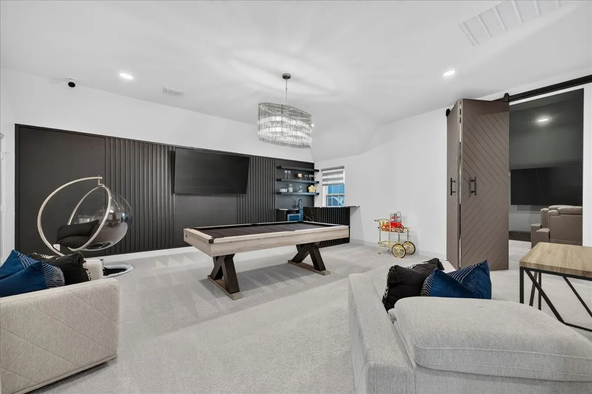 Spacious recreational room featuring light-toned carpeting and a contemporary chandelier